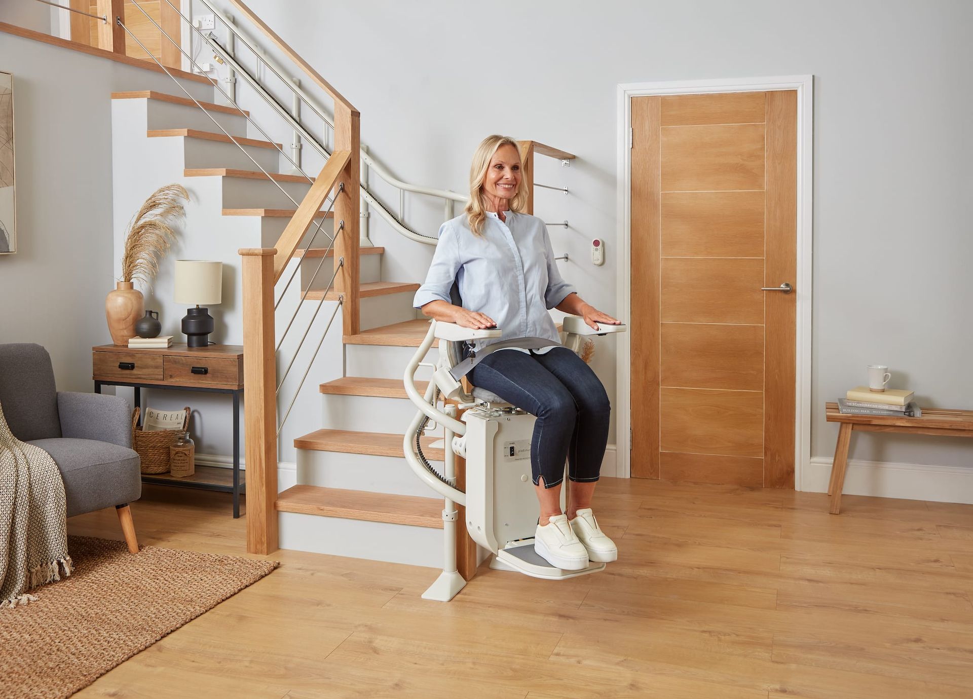 Person sitting on a white stair lift in a bright home interior with wooden floors and stairs