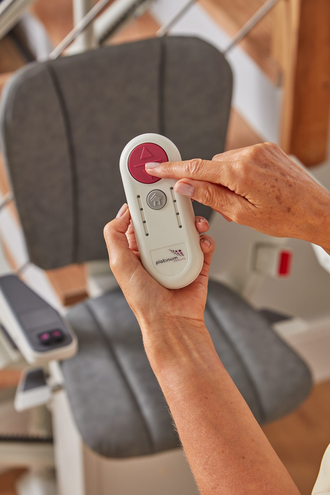 Hands holding a white remote controller with a red dial in front of a gray chair.
