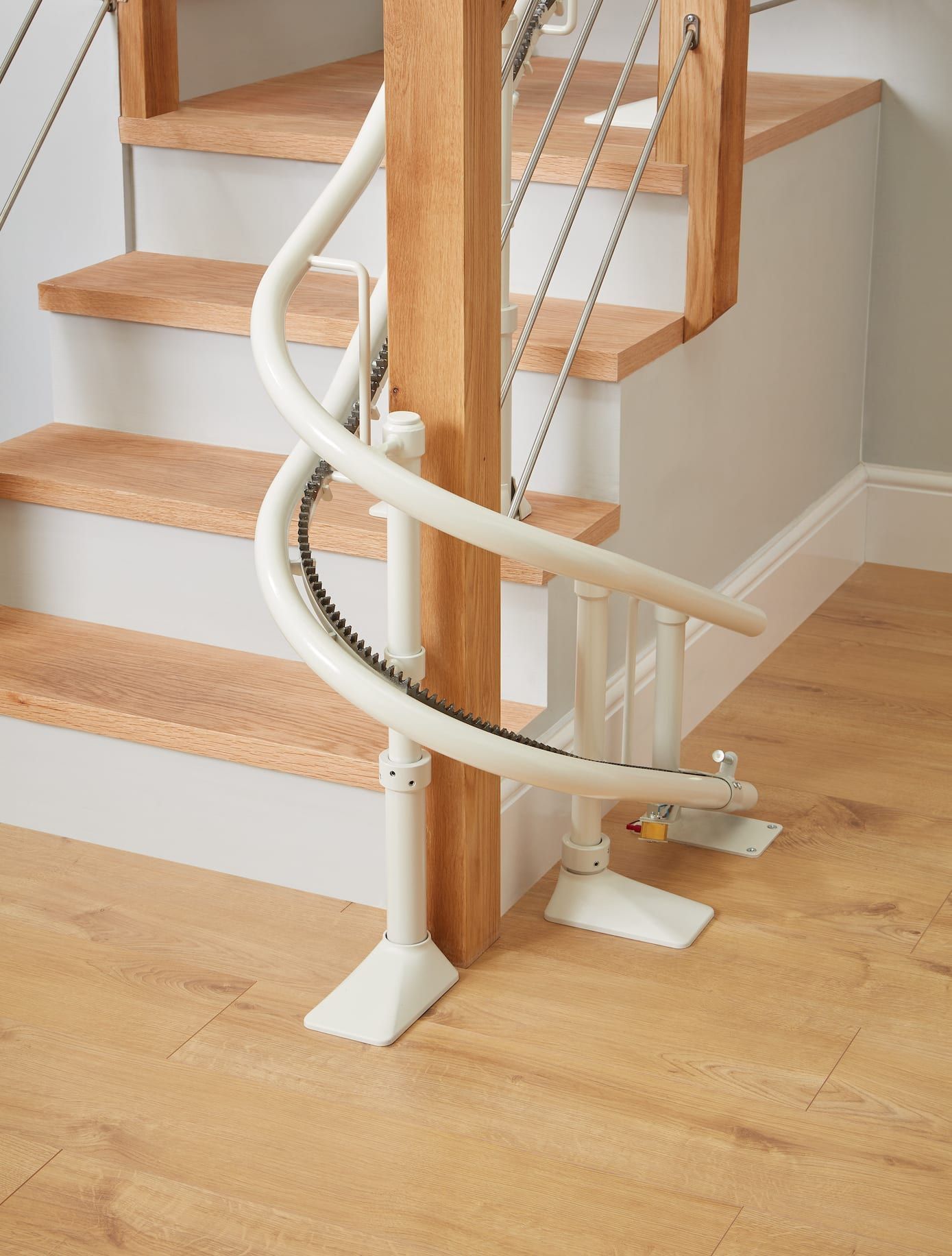 Curved white stair lift beside wooden stairs in a home interior
