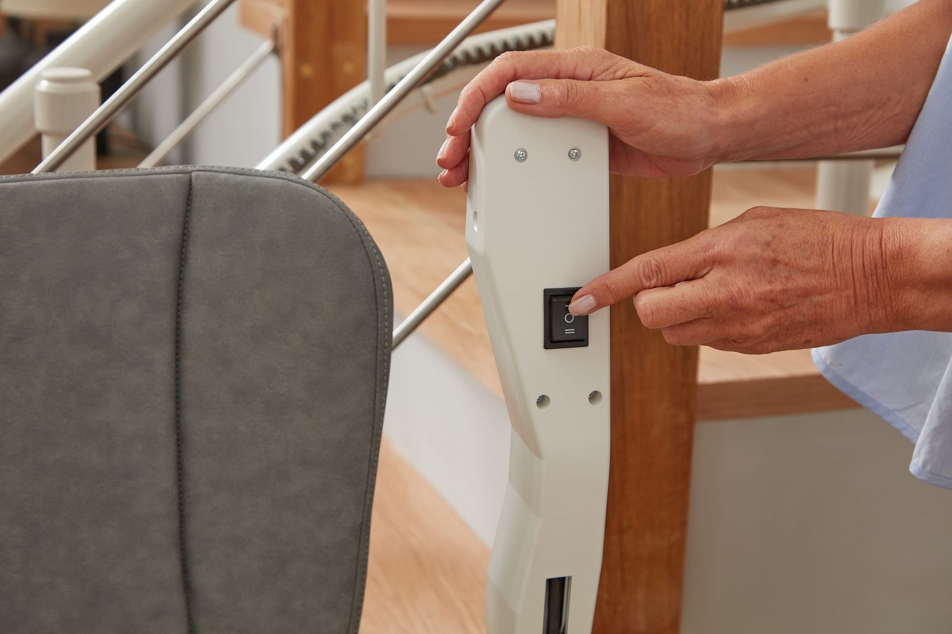 Hand turning a wall-mounted light switch beside a staircase and gray chair.
