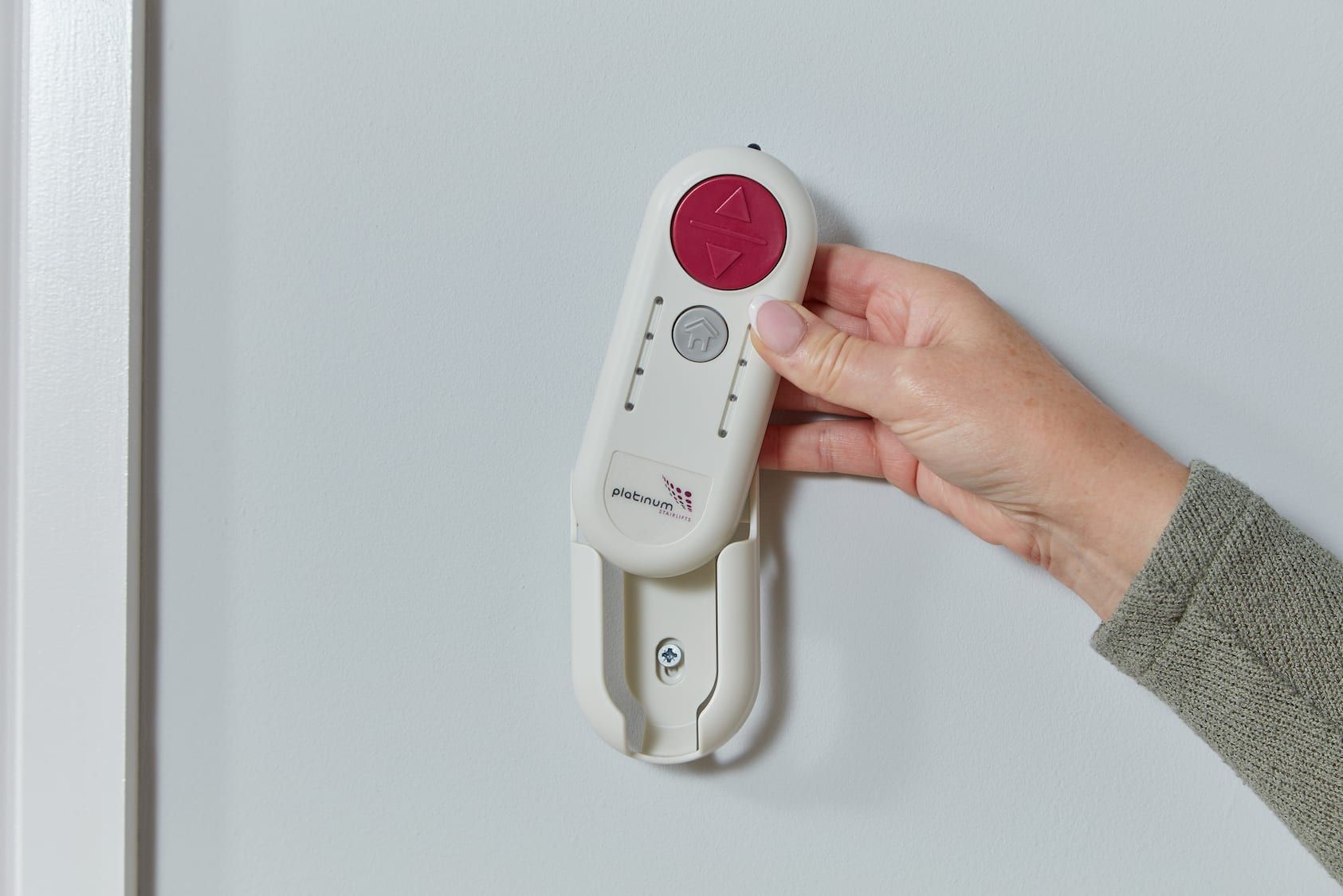 Hand holding a wall-mounted white emergency call device with a red button