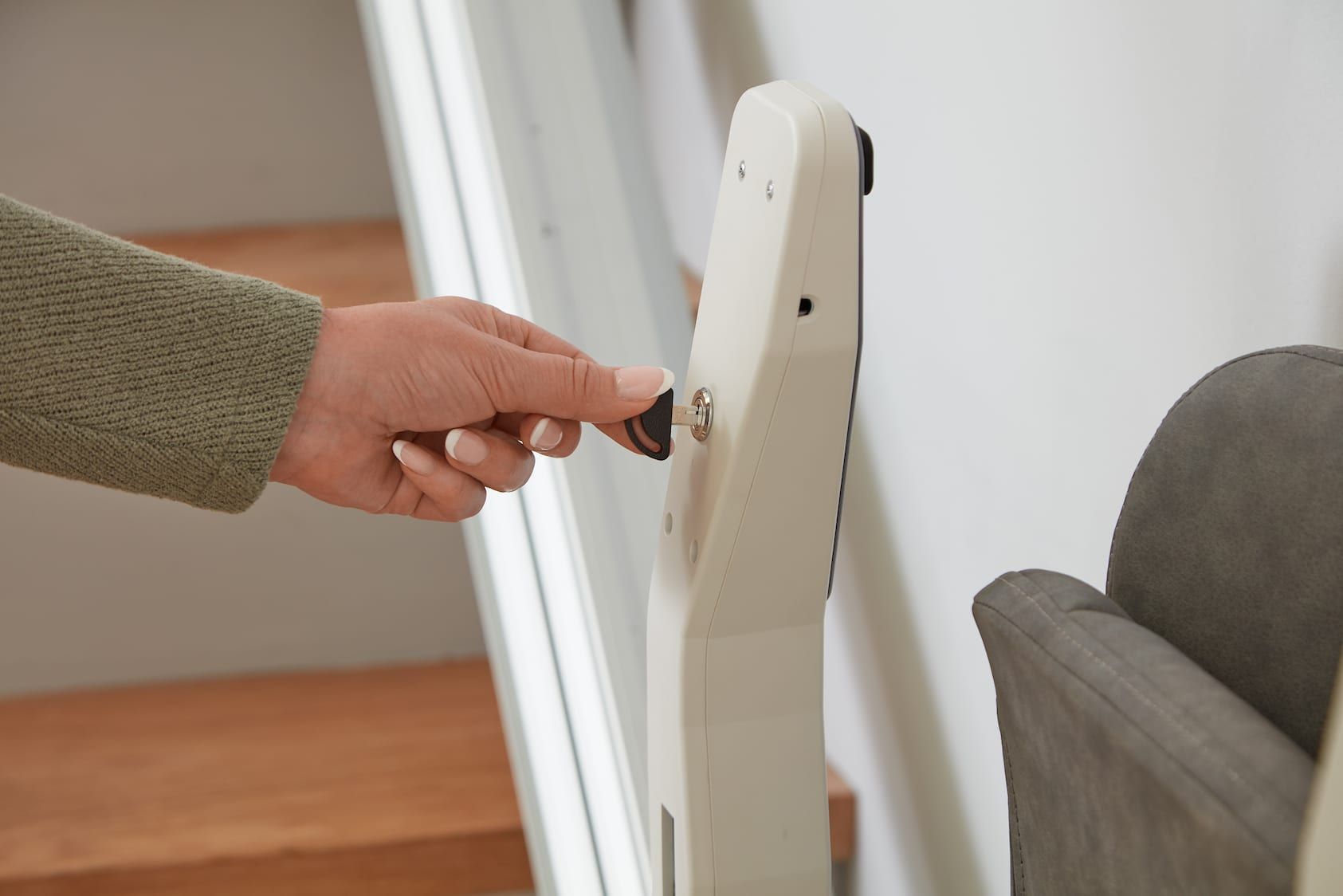 Hand turning the latch on a white folding gate beside a gray sofa.