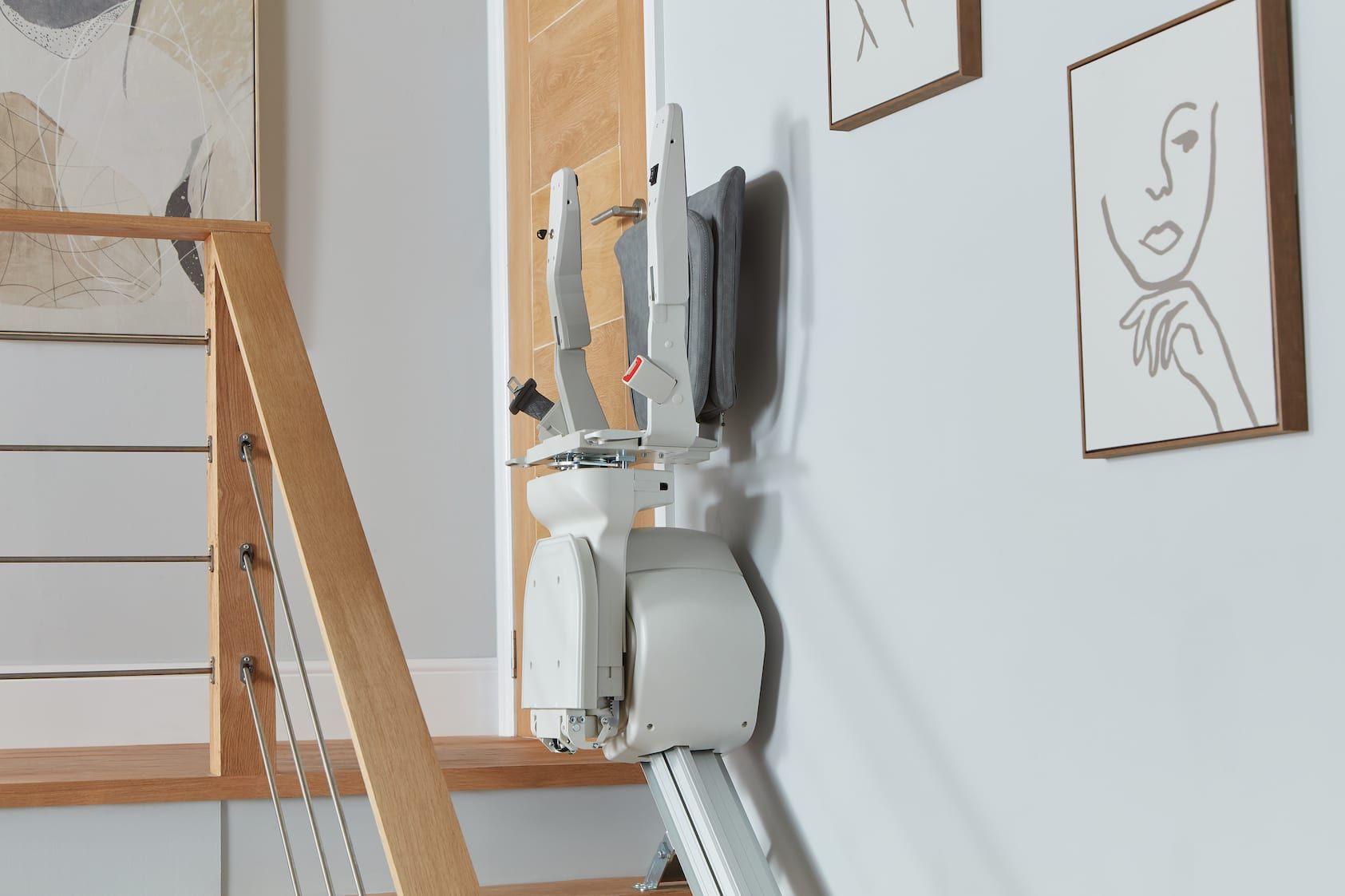 Staircase in a bright hallway with a mounted vacuum and framed line drawings on the wall