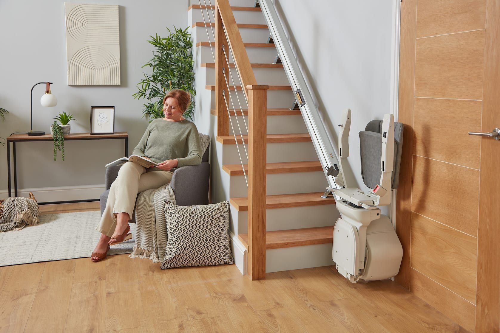 Woman sitting in a living room beside a wooden staircase and stair lift