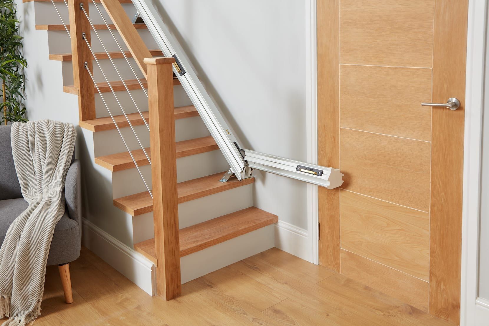 Stairlift beside wooden stairs in a home hallway, with white rail and folded seat near a door