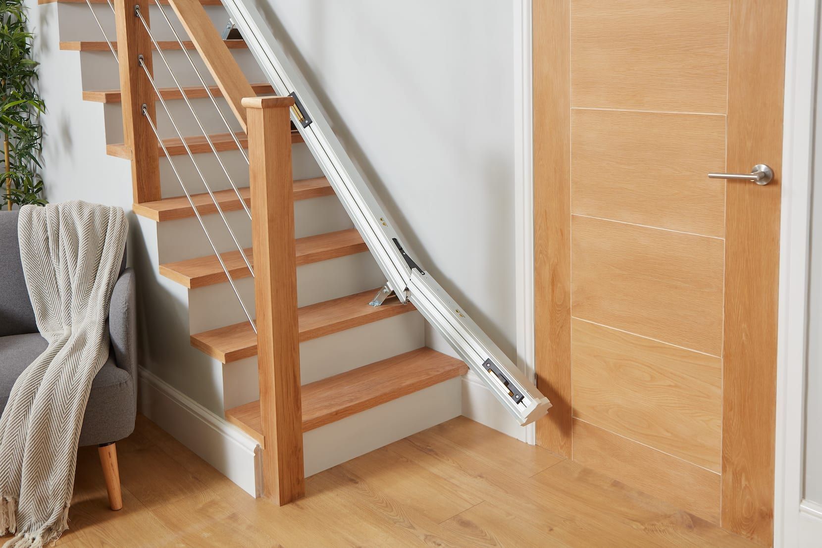 Indoor staircase with a stairlift beside a wooden door and gray chair in a home interior