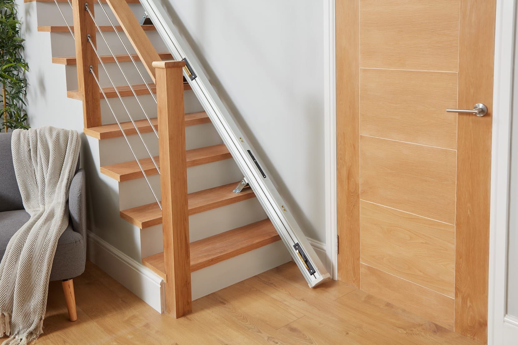 Indoor staircase with a wooden handrail and a silver ladder leaning against it next to a closed wooden door.