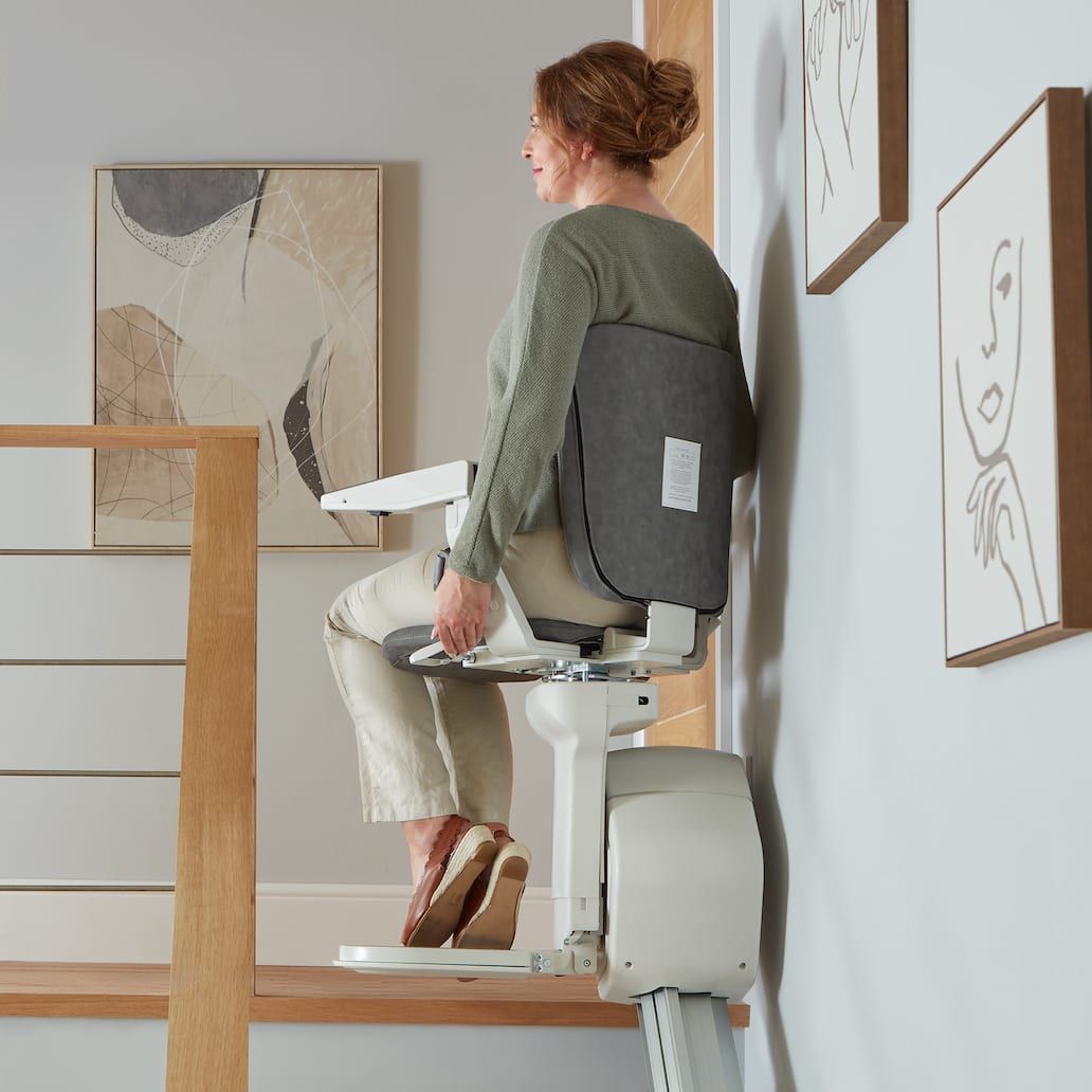 Woman seated on a stairlift beside a staircase in a bright home interior
