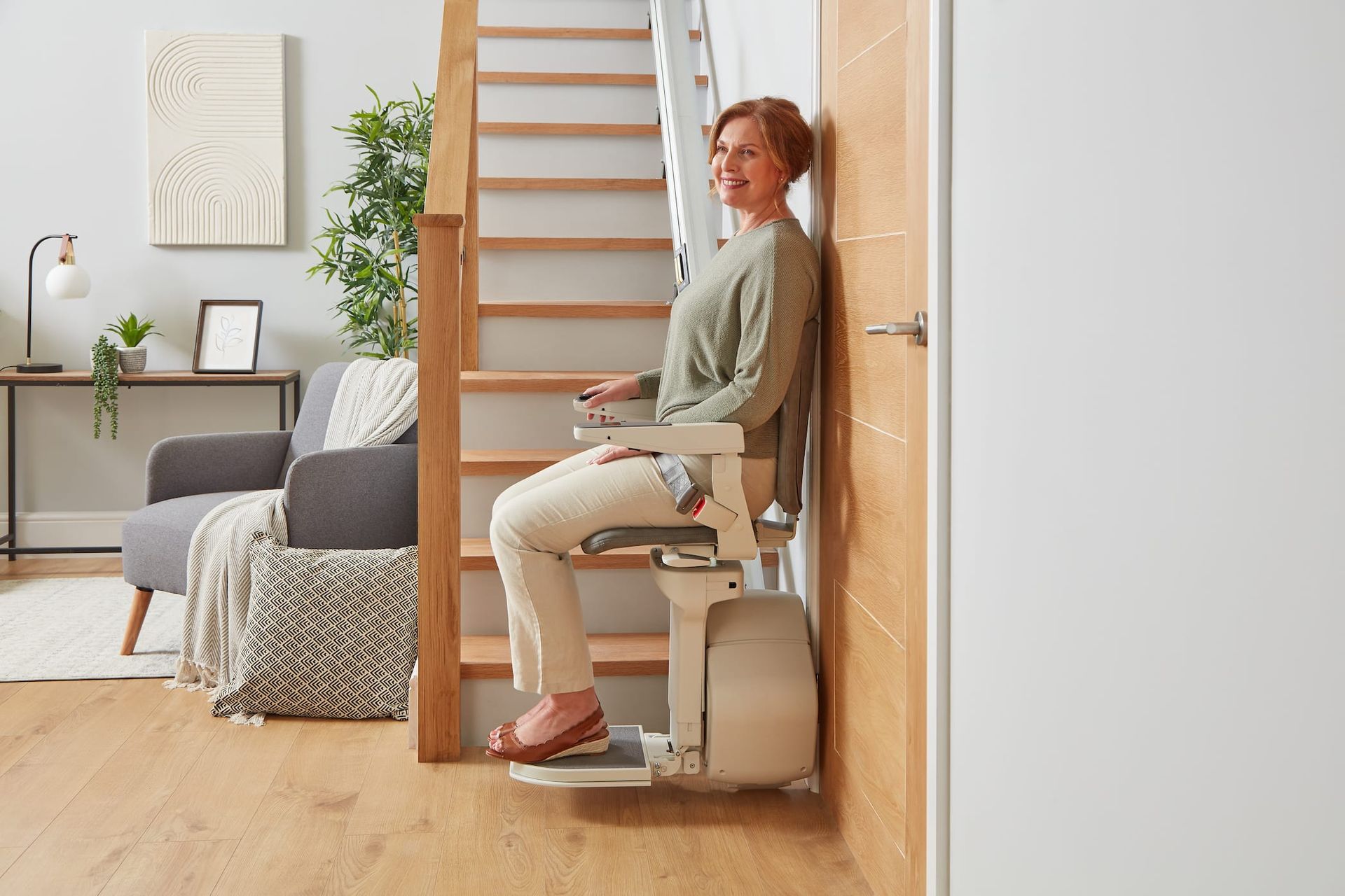Woman seated on a stairlift in a bright home interior, with stairs and living room nearby