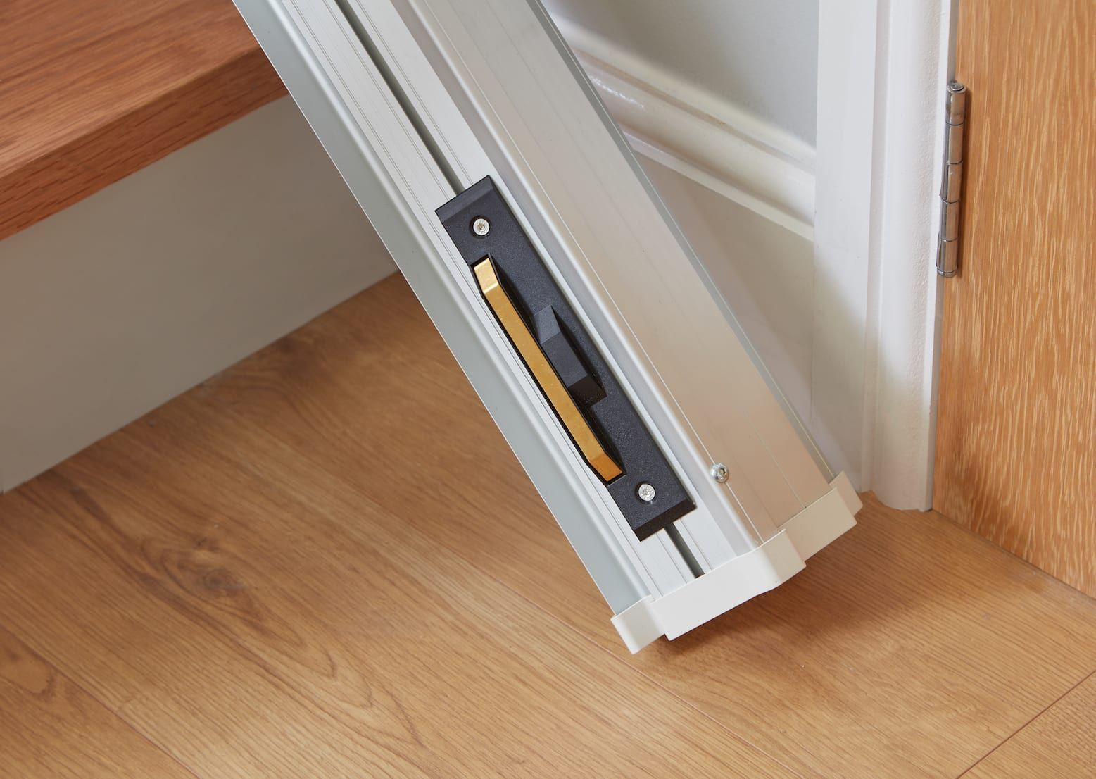 Close-up of a white door bottom seal near a wooden floor and door frame