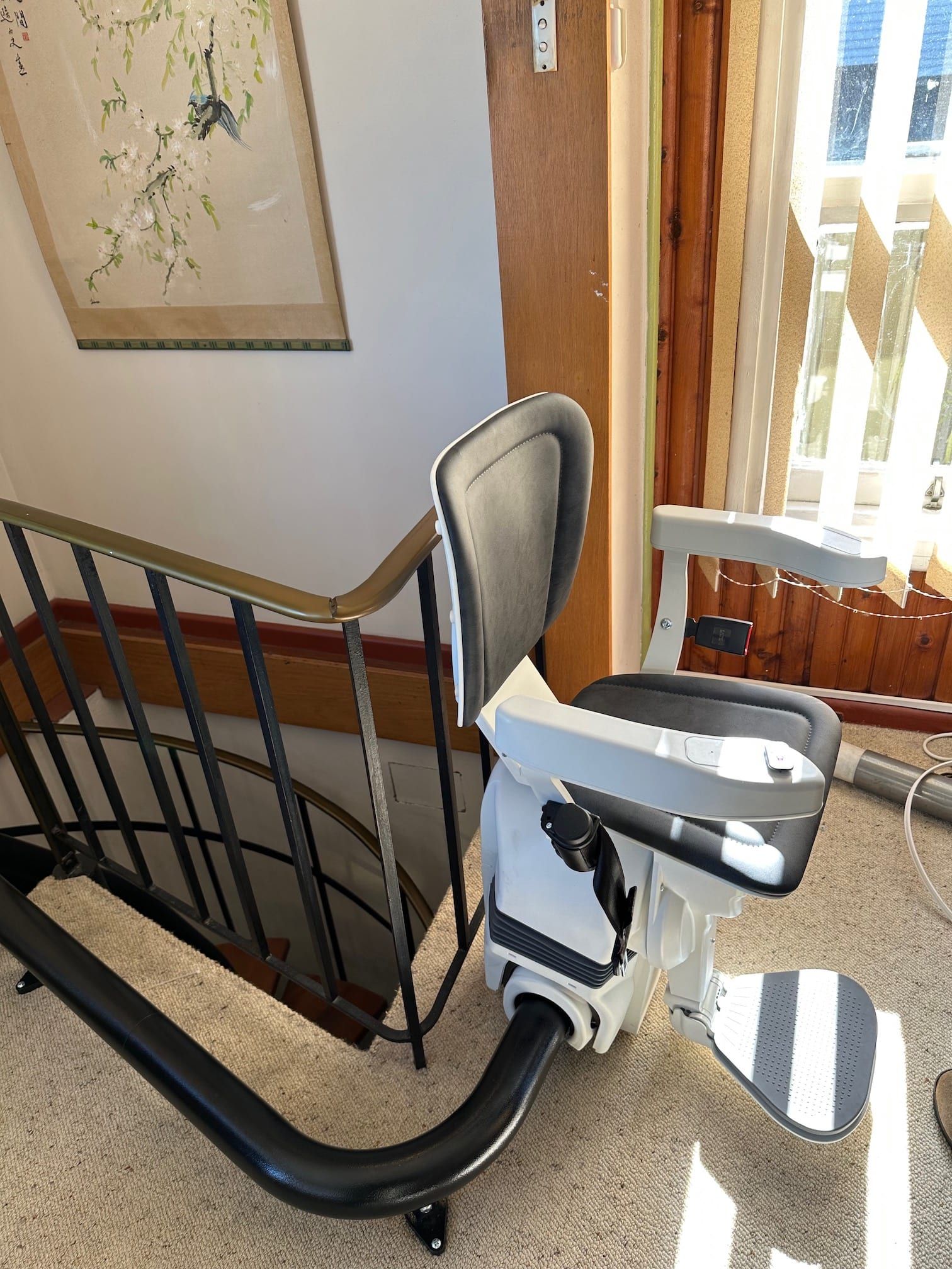 Stairlift chair beside a carpeted stairway near a bright window and wooden railing.