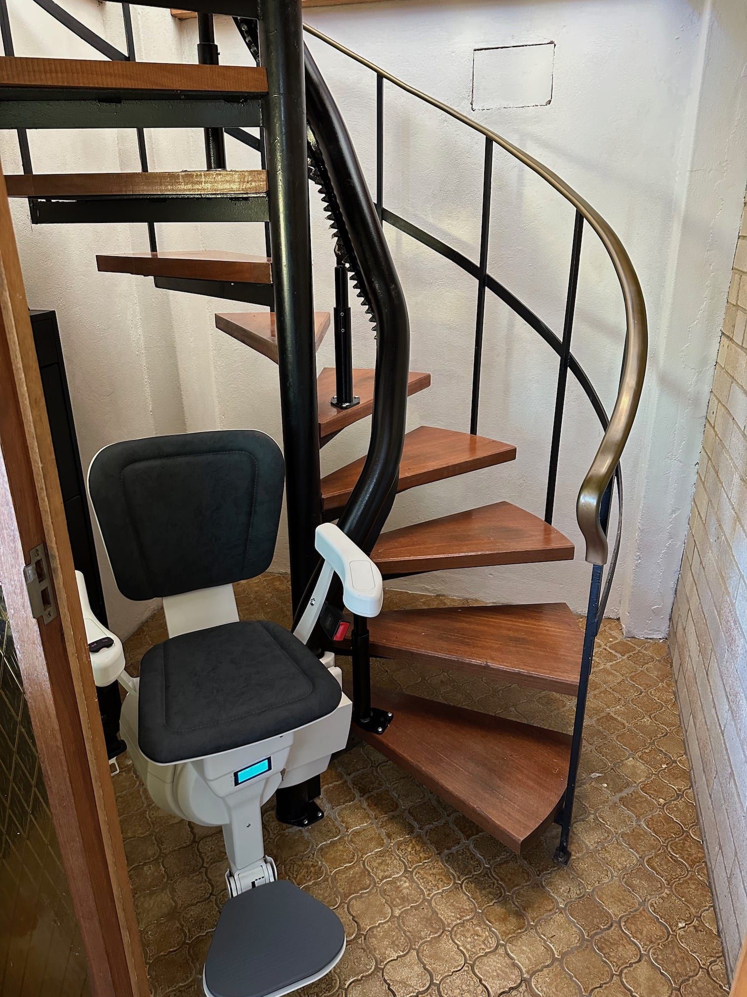Curved stairlift on a narrow wooden staircase with black railings and a gray seat