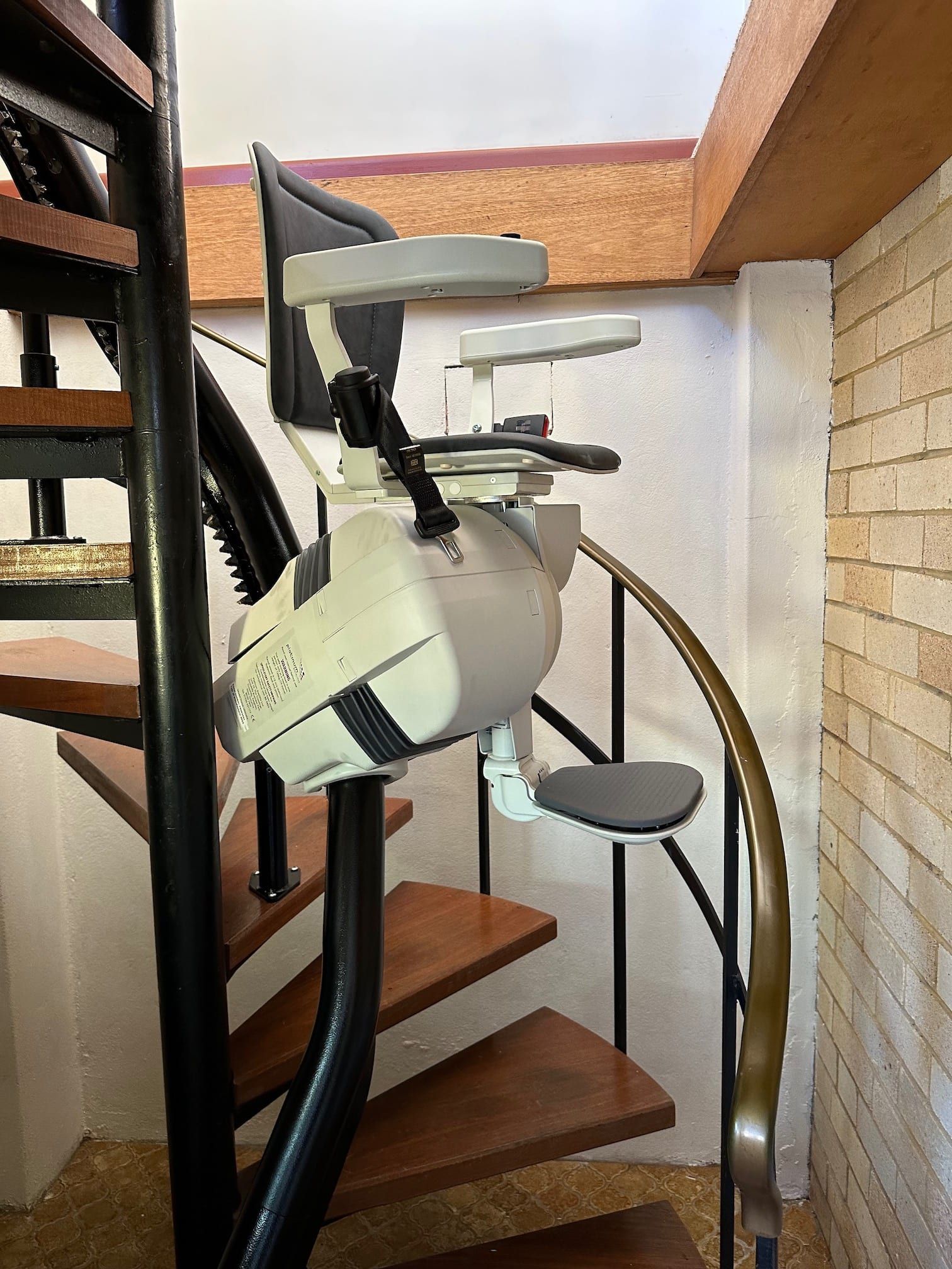 Stairlift installed on a narrow indoor staircase with wooden steps and metal railings.