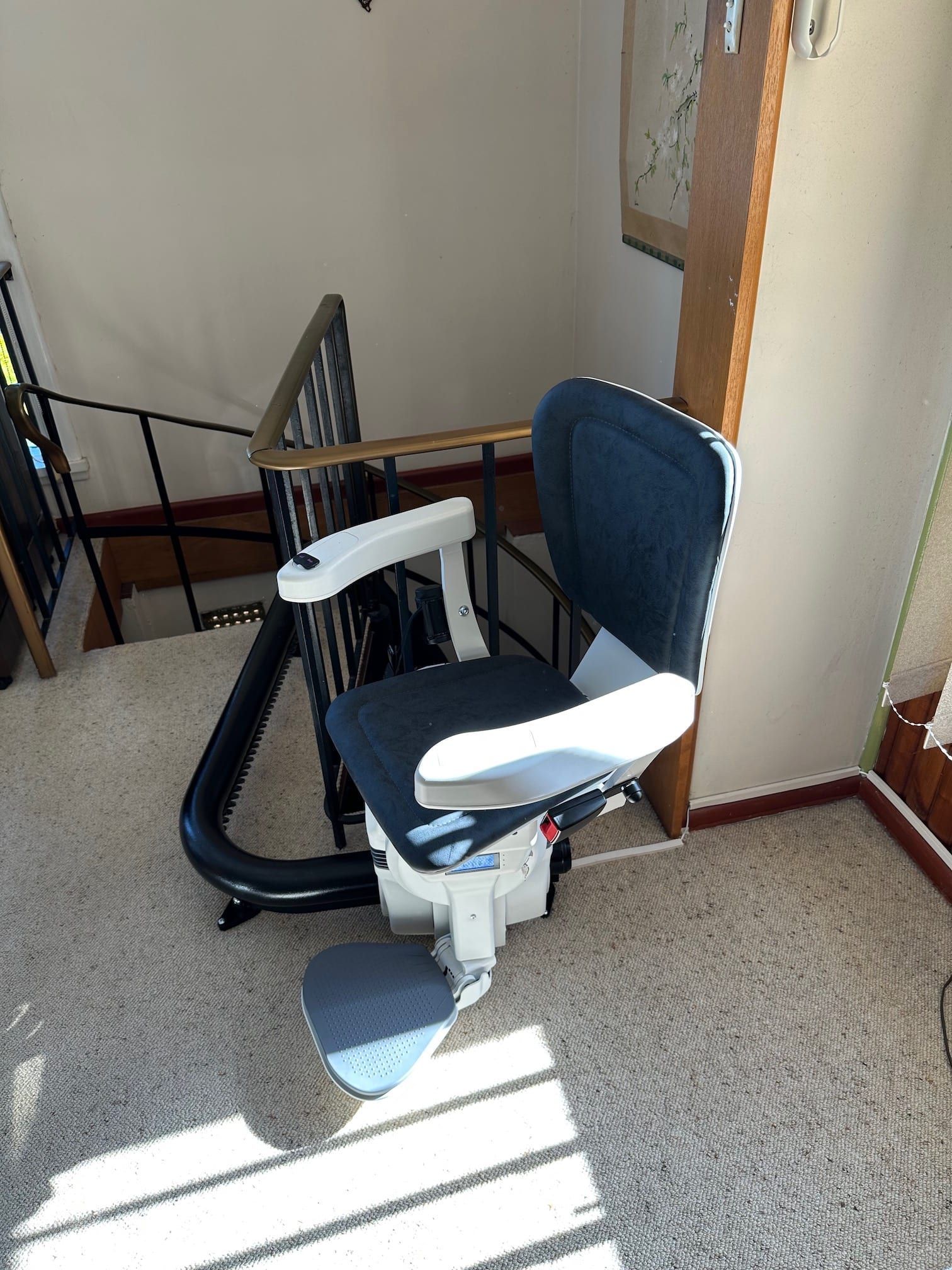Blue office chair by a wall in a sunlit room, with a stair rail and framed board nearby