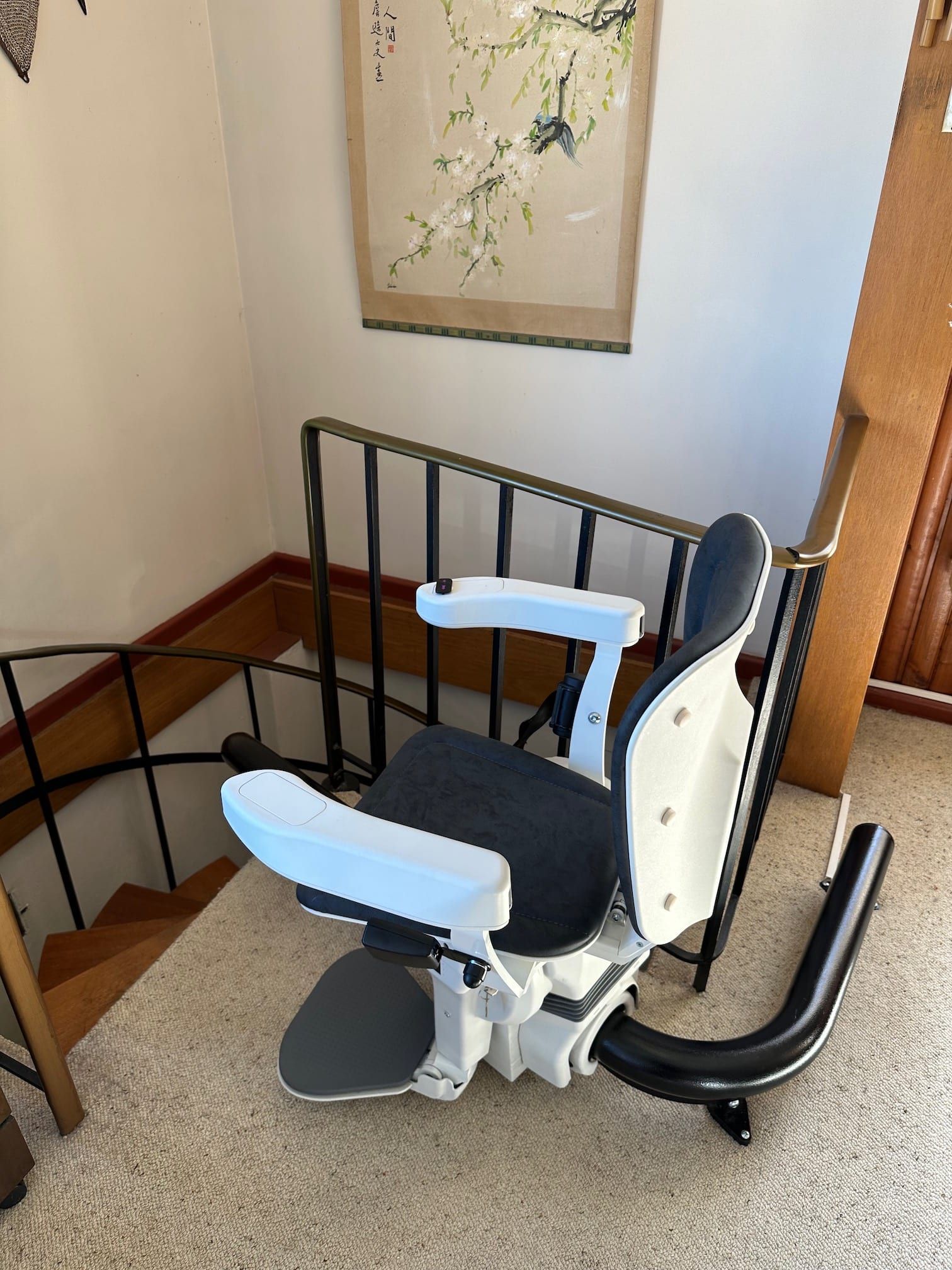 Stair lift chair mounted beside carpeted stairs with black railings in a home hallway
