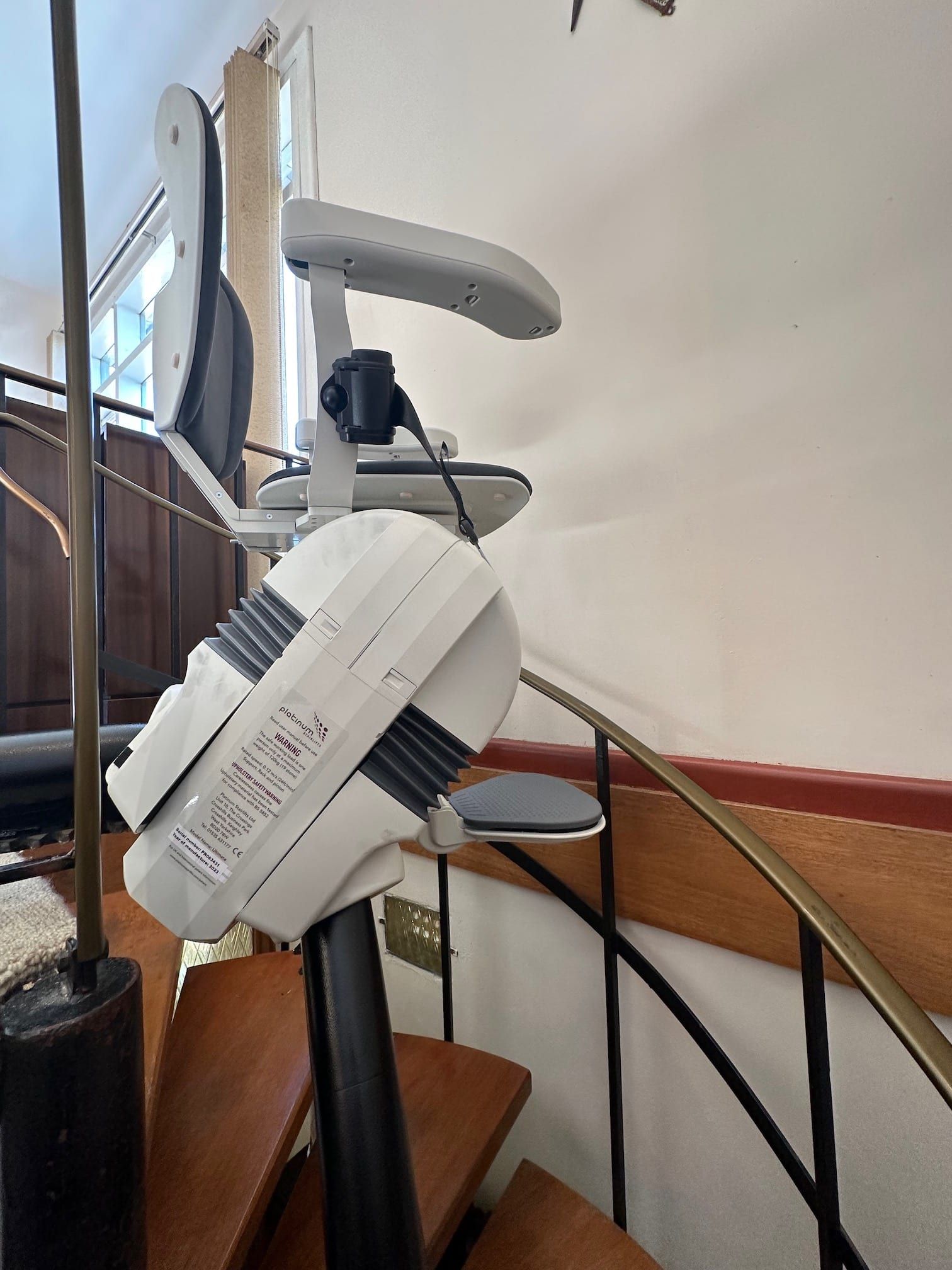 White modem/router mounted on a stair railing beside cables and a wooden banister indoors