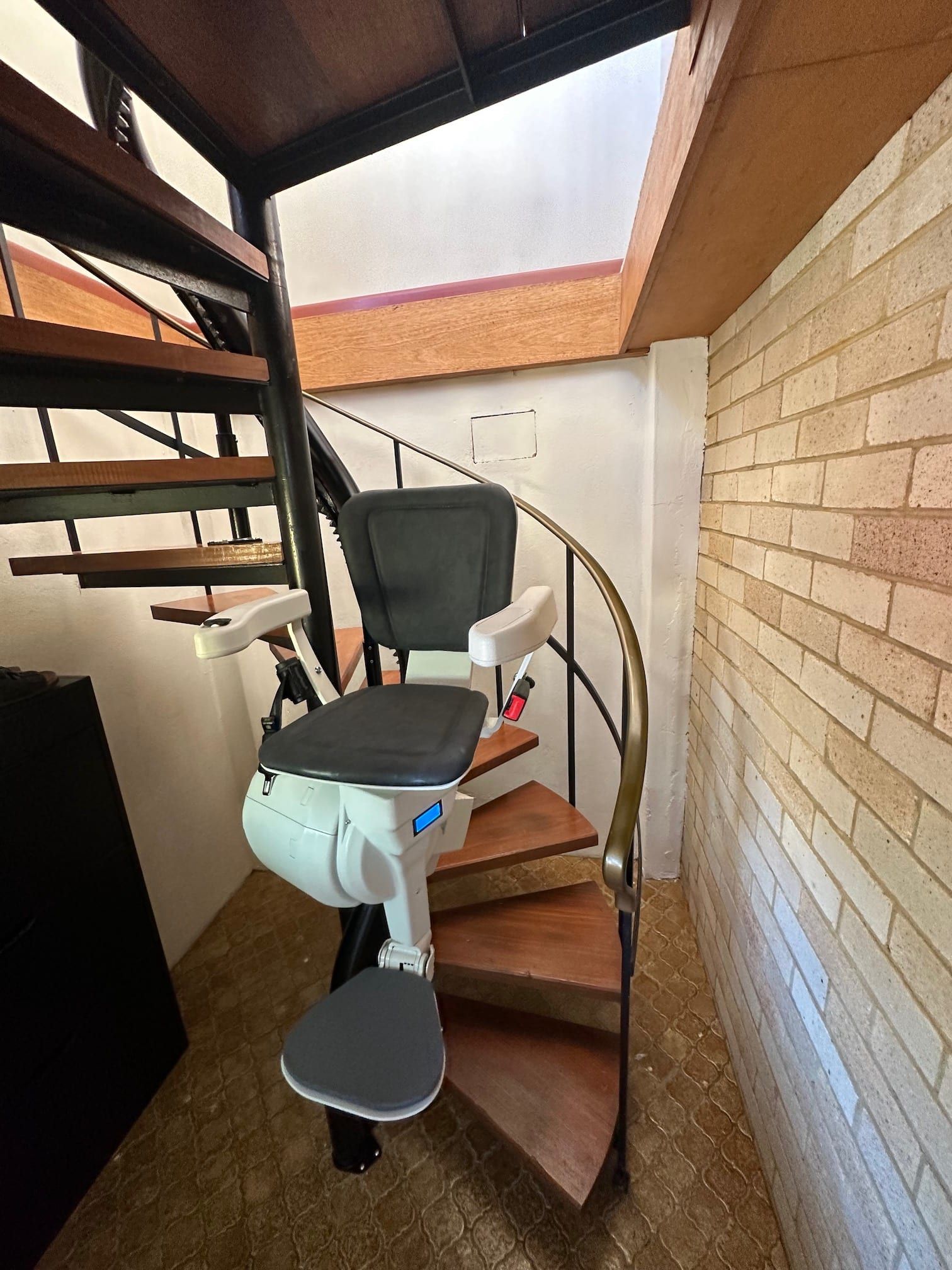 Motorized stairlift on a narrow spiral staircase beside a brick wall