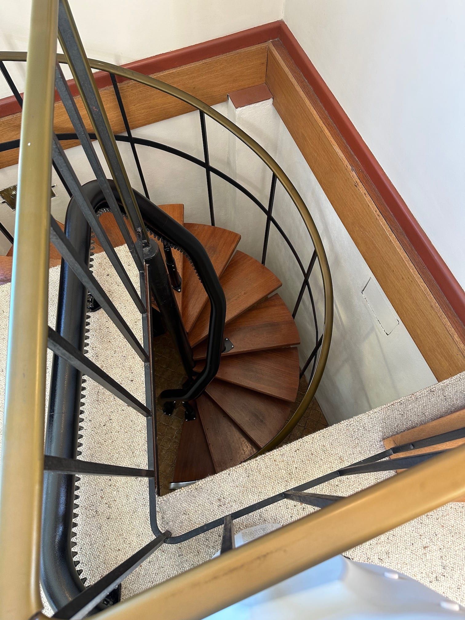 Top-down view of a spiral staircase with wood steps, black railing, and beige walls.