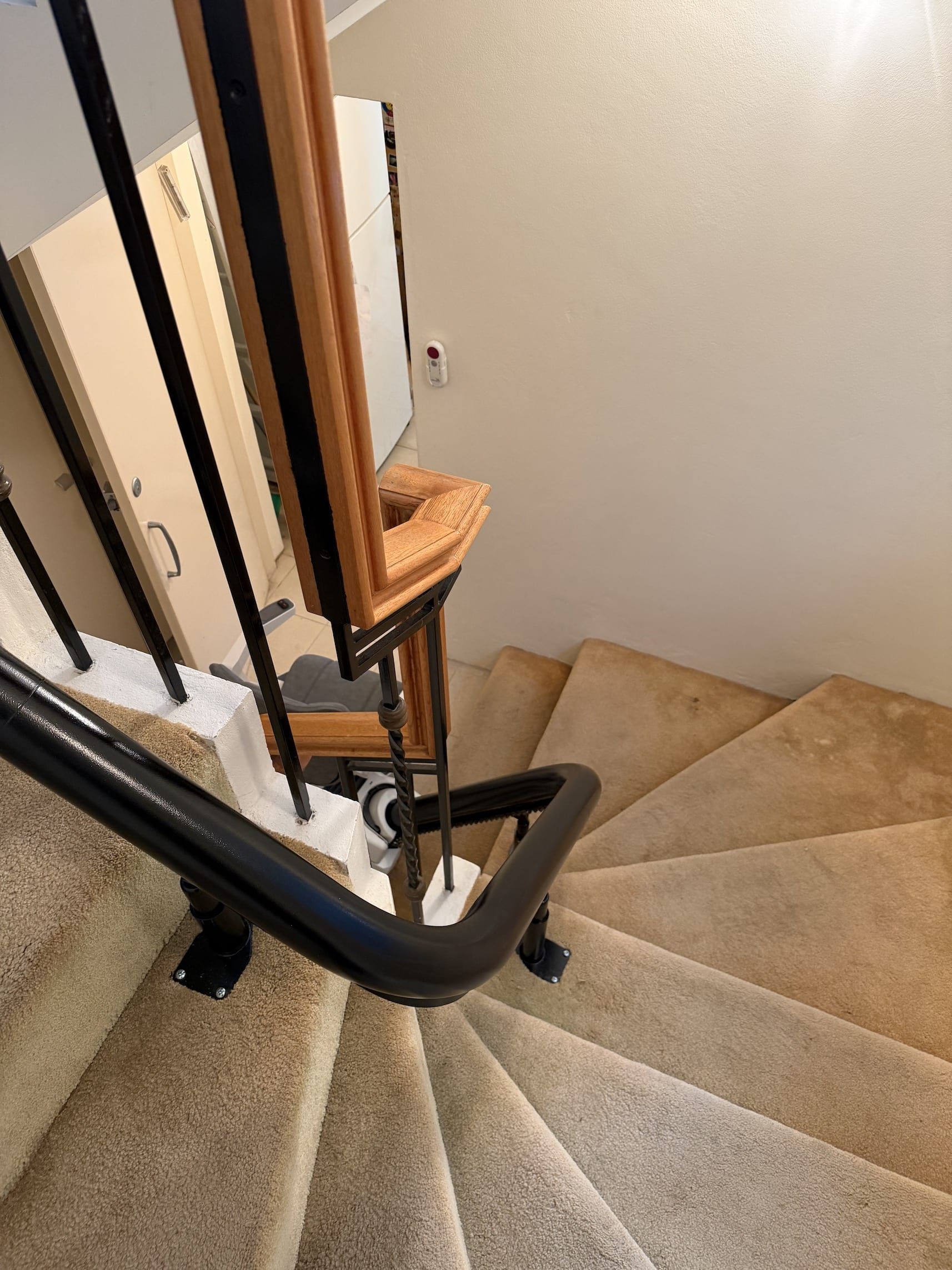 Spiral staircase with beige carpet and black handrail inside a home.