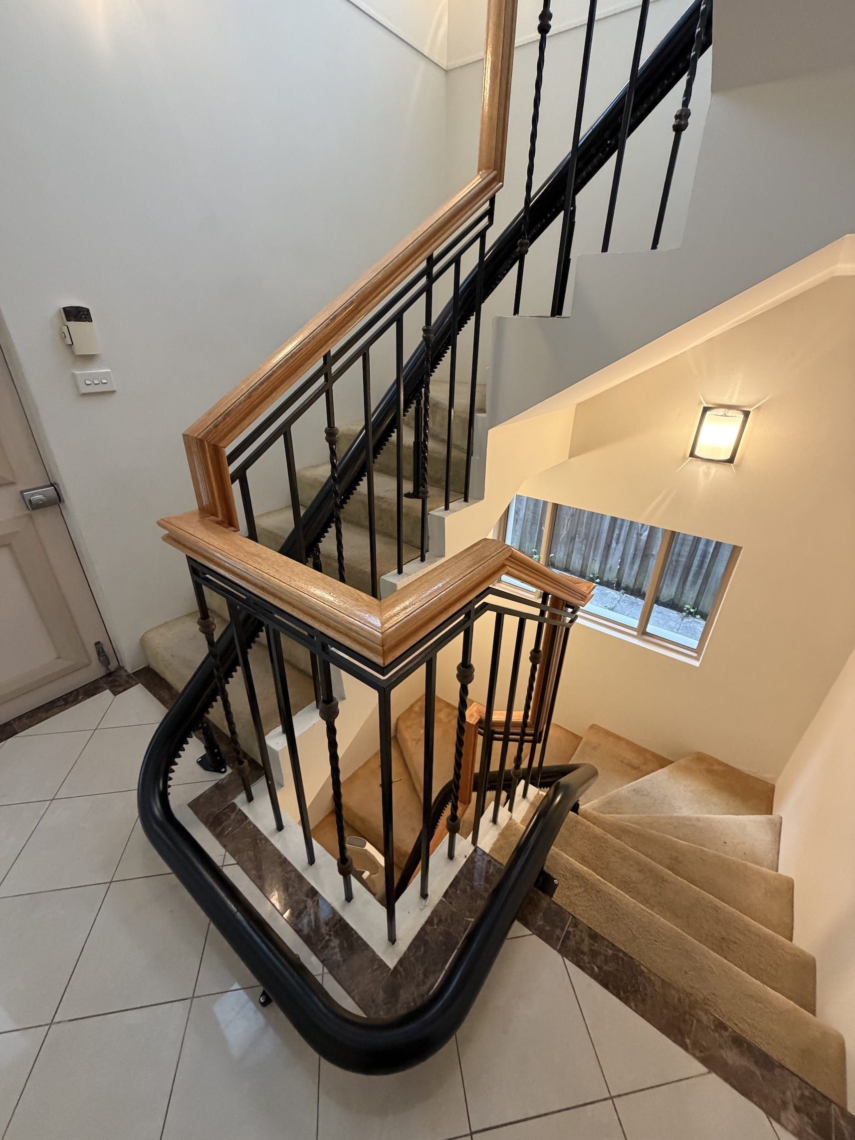 Indoor stairwell with beige carpeted steps, black railing, and white tile floor around a landing.
