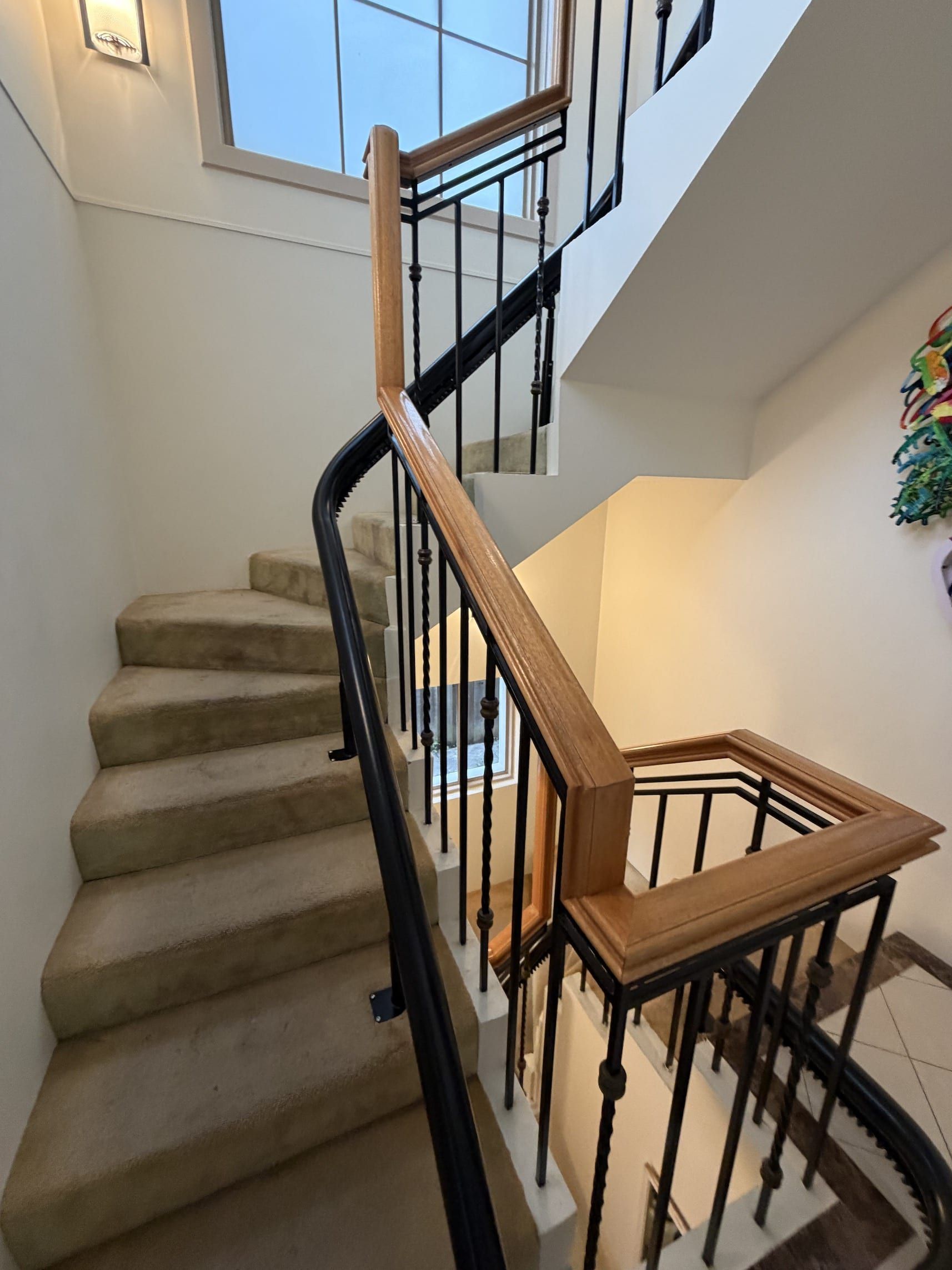 Carpeted staircase with wooden handrail and black iron balusters in a bright home interior