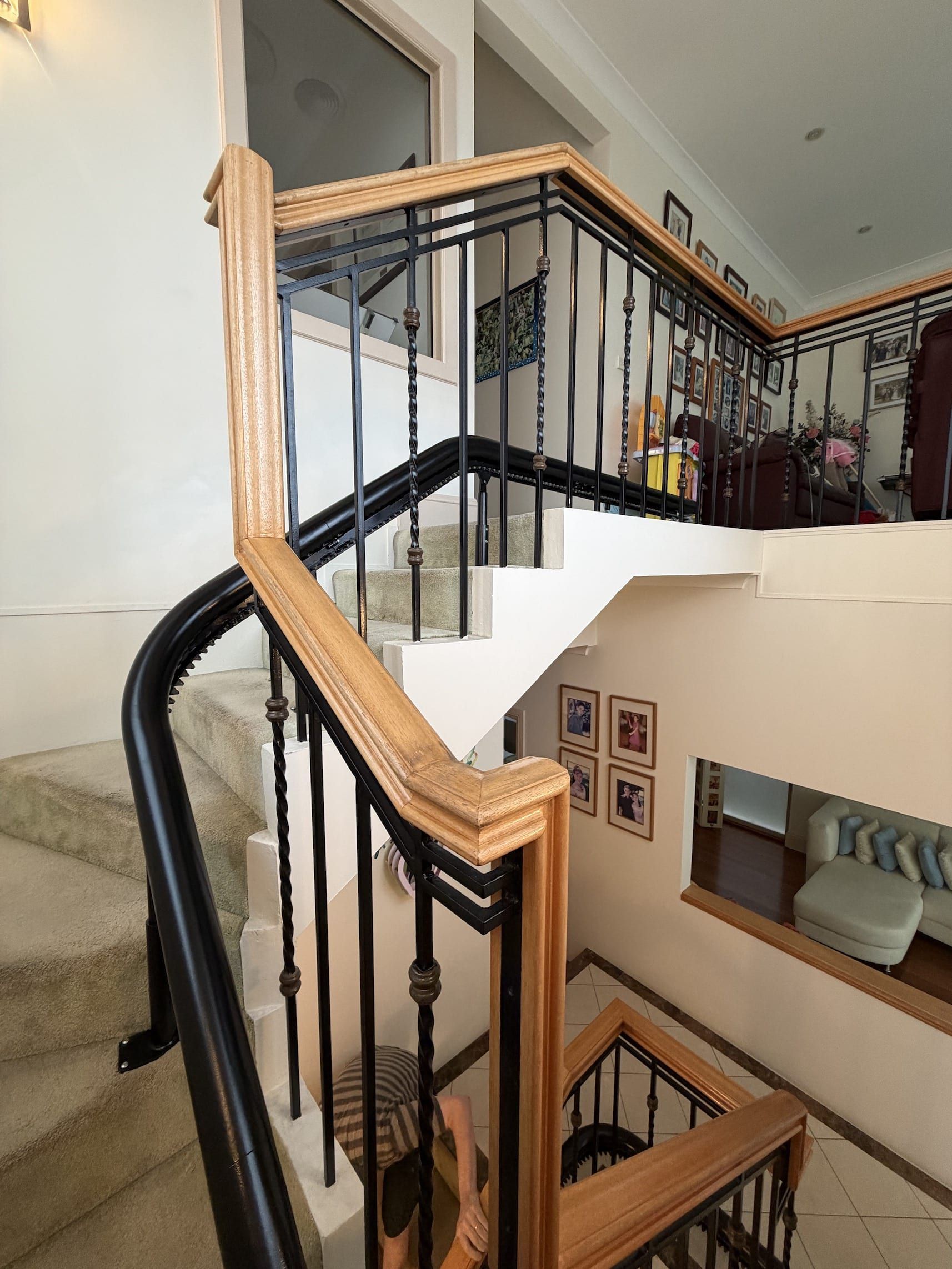 Curved indoor staircase with black iron railing and light wood banister, viewed from an upper landing.