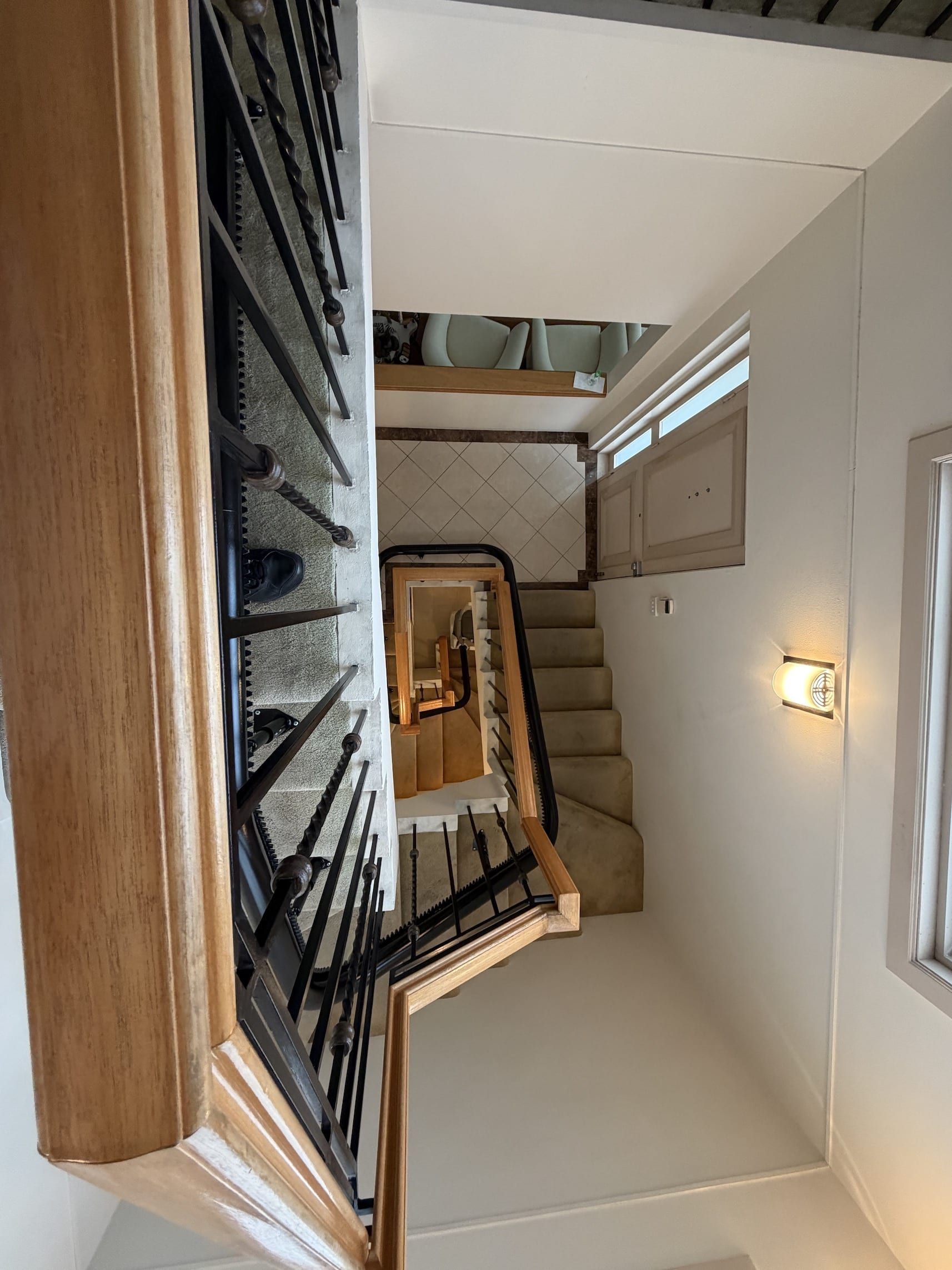 Staircase landing with black railing, beige steps, and white walls viewed from above.