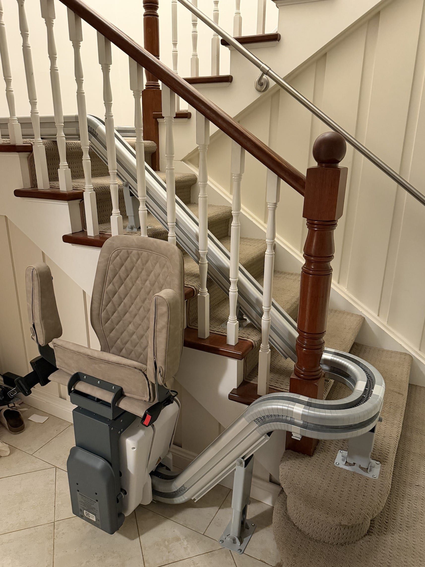Curved stair lift beside a carpeted staircase with beige walls and wooden banister
