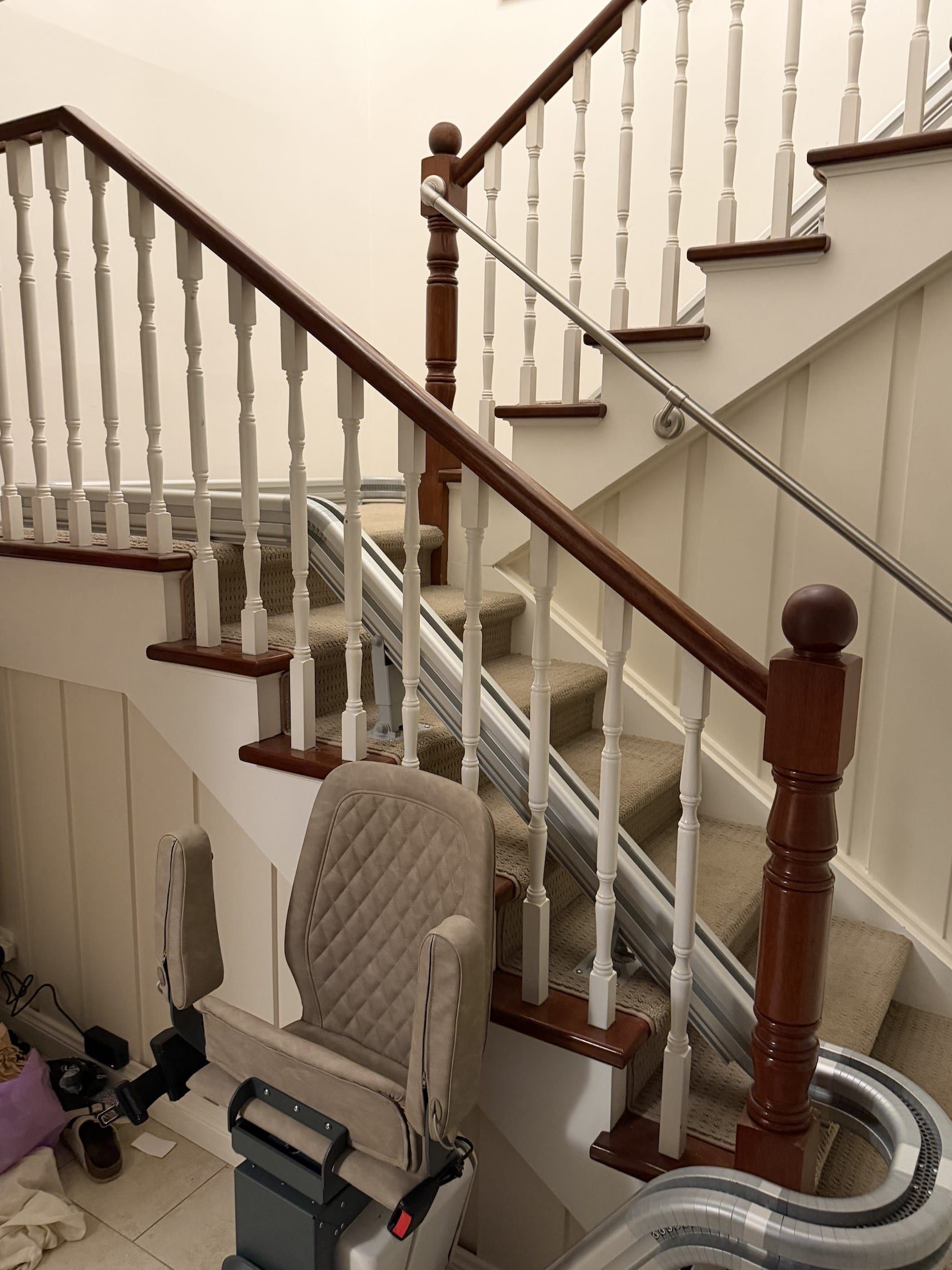 Indoor staircase with beige walls, white balusters, dark wood handrail, and a chair at the bottom.