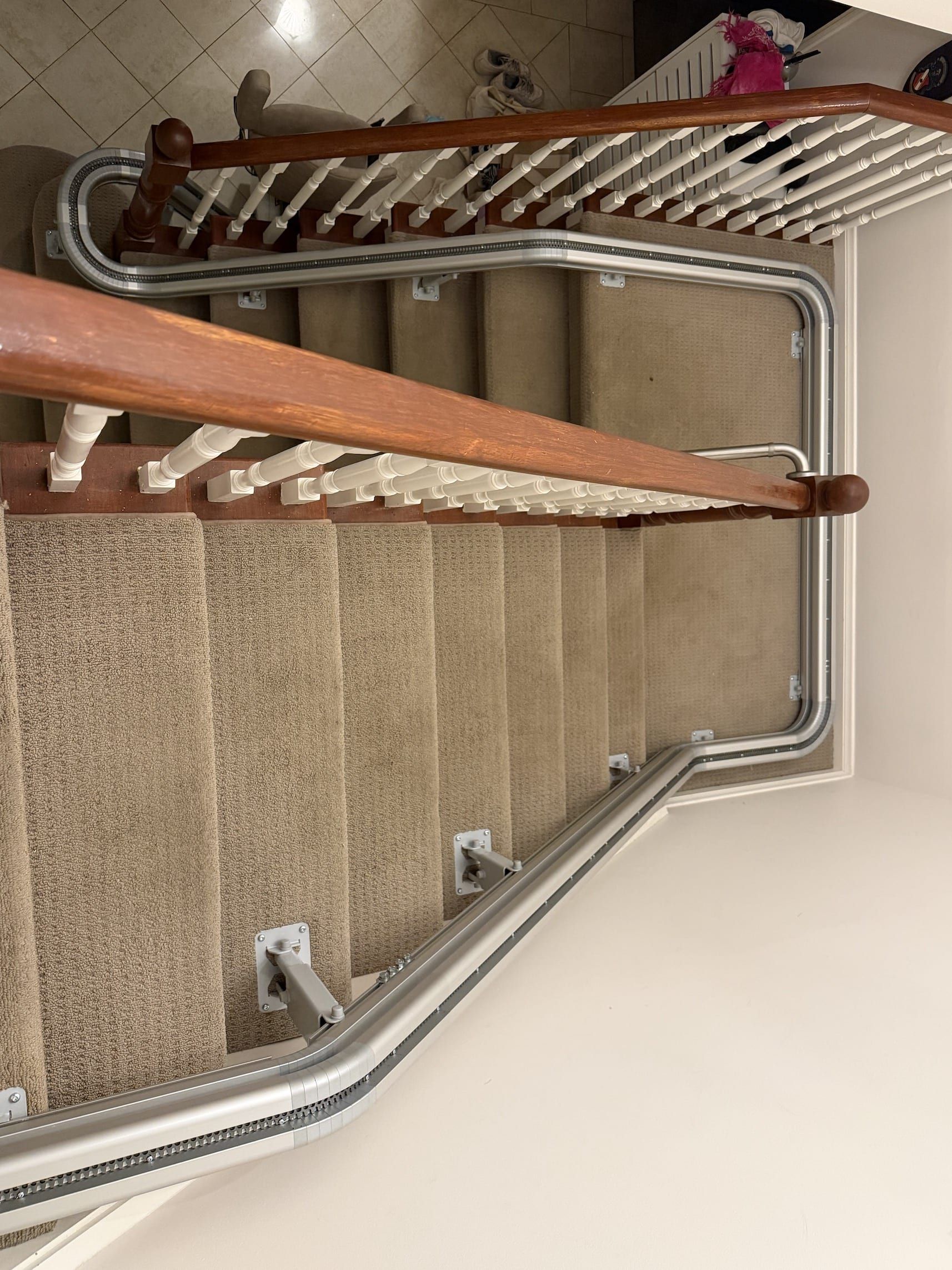 Indoor staircase with tan carpet, metal railings, and wooden banister, viewed from above.