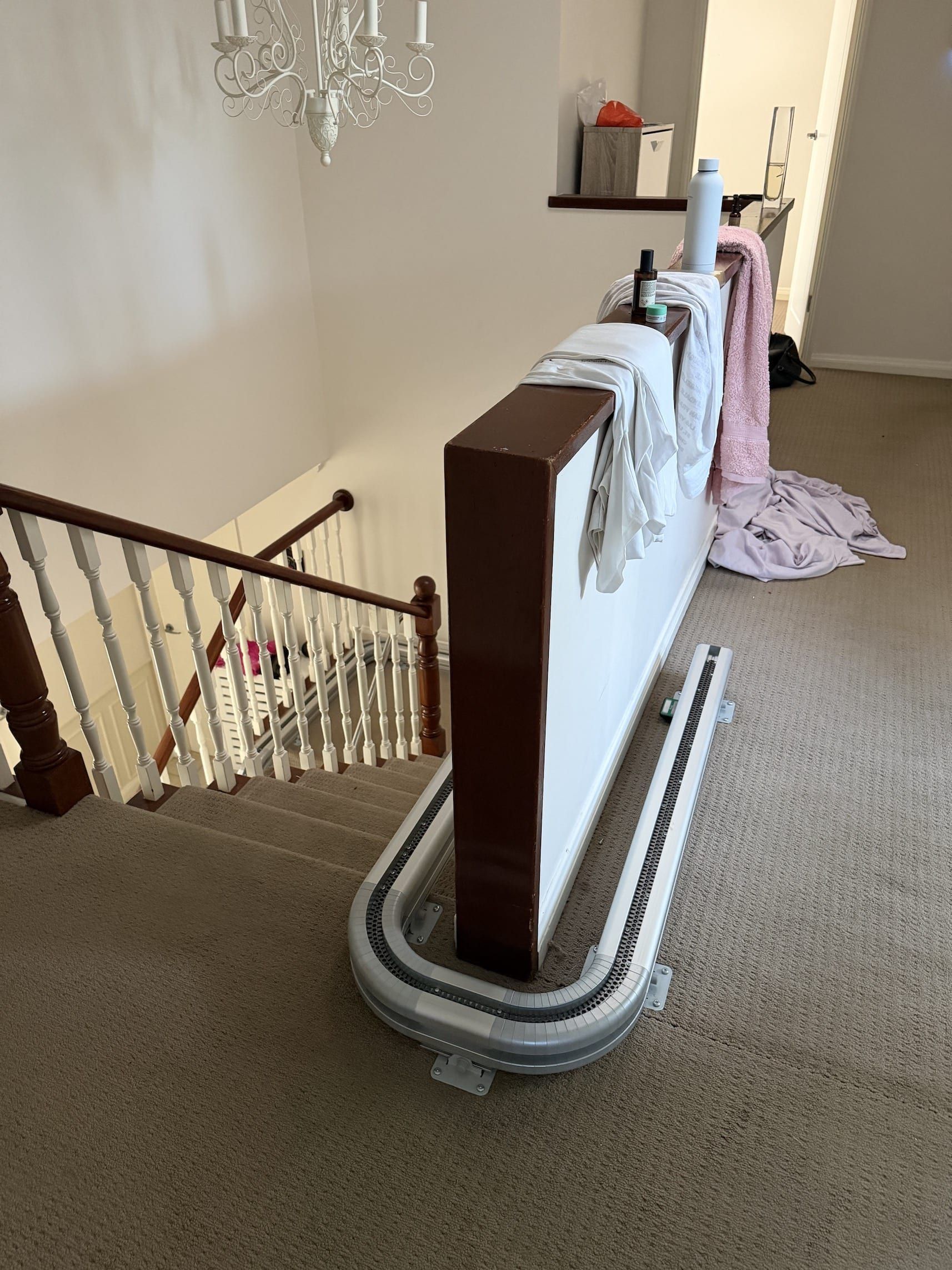 Carpeted staircase landing with a stair lift rail beside the banister and a draped blanket on the upper floor