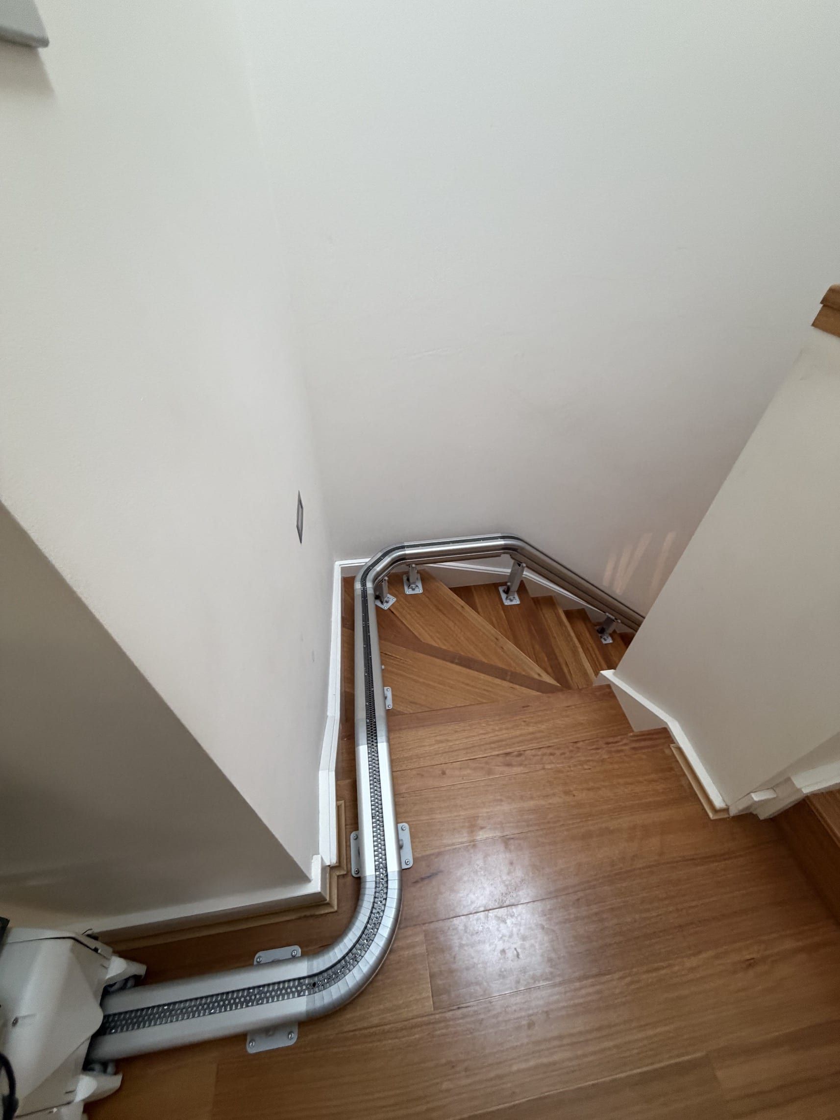 Winding white cable conduit along a stairwell corner with wood flooring and white walls