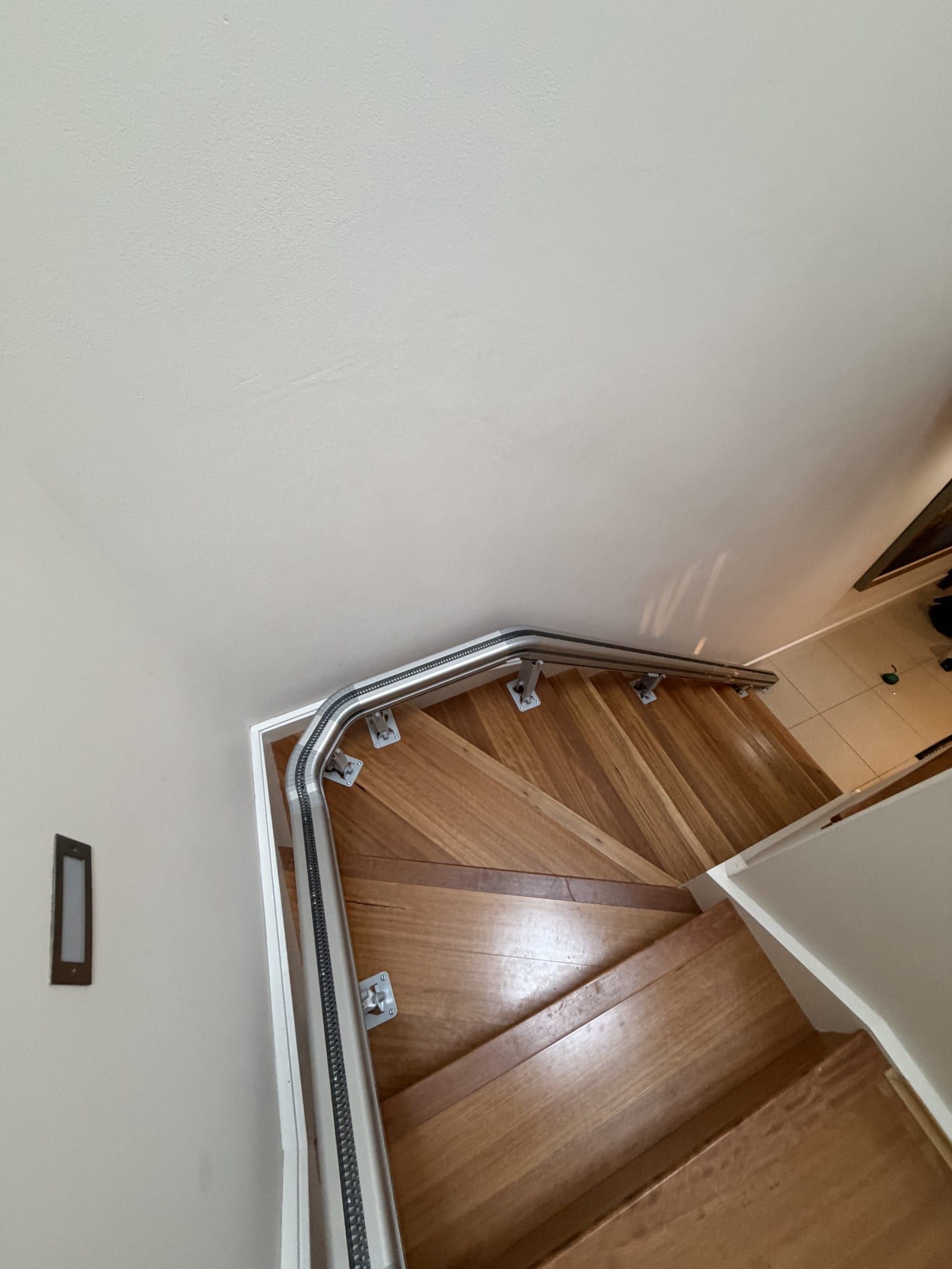 Curved wooden staircase viewed from above, with white walls and a handrail along the landing.