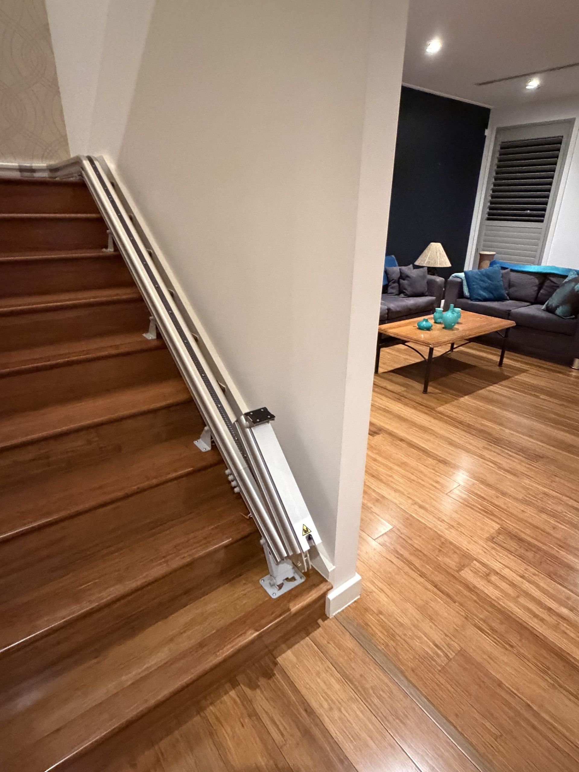 Indoor staircase with metal railing beside a hardwood-floored living room with blue sofa and coffee table