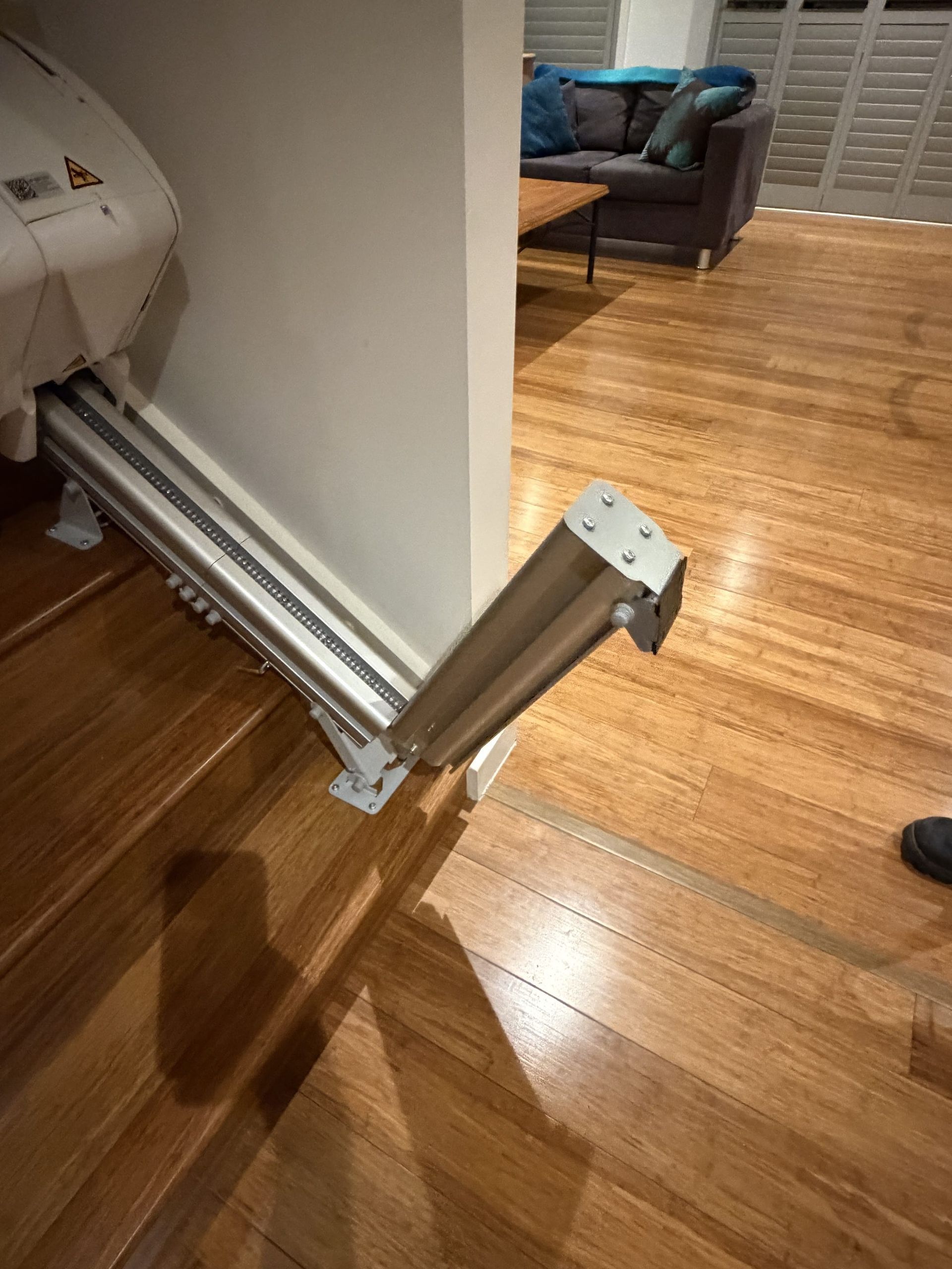 White wheelchair-mounted metal support arm extending over a hardwood floor in a living room