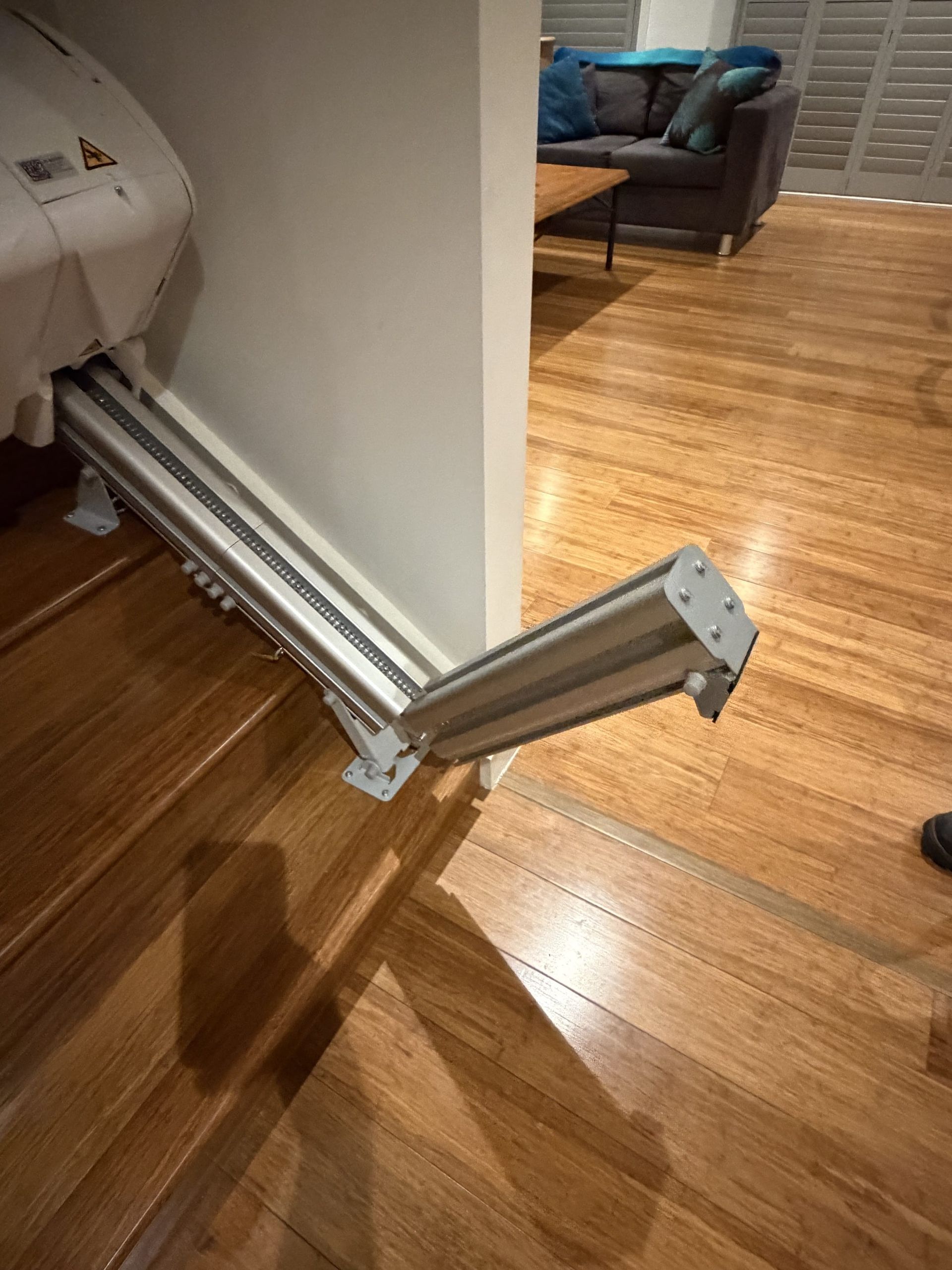 Foldable silver wheelchair ramp extending from a doorway onto a hardwood floor in a home.