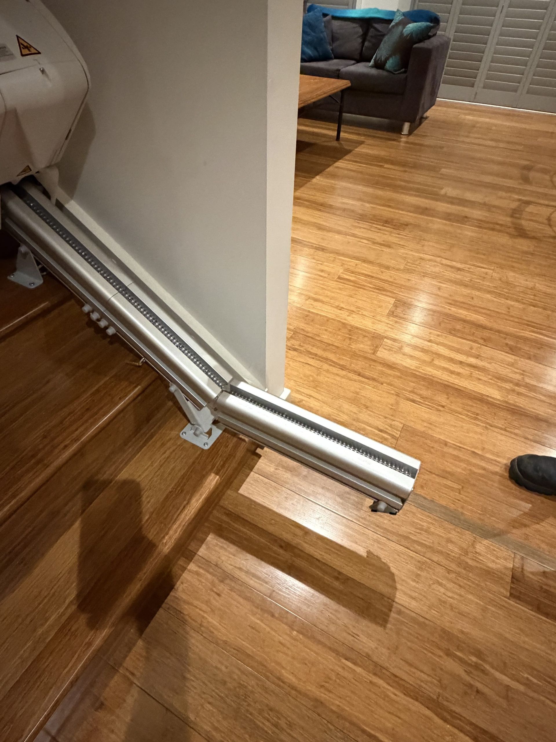 Metal wall-mounted pipe assembly running along a hallway with hardwood floors and a sofa in the background