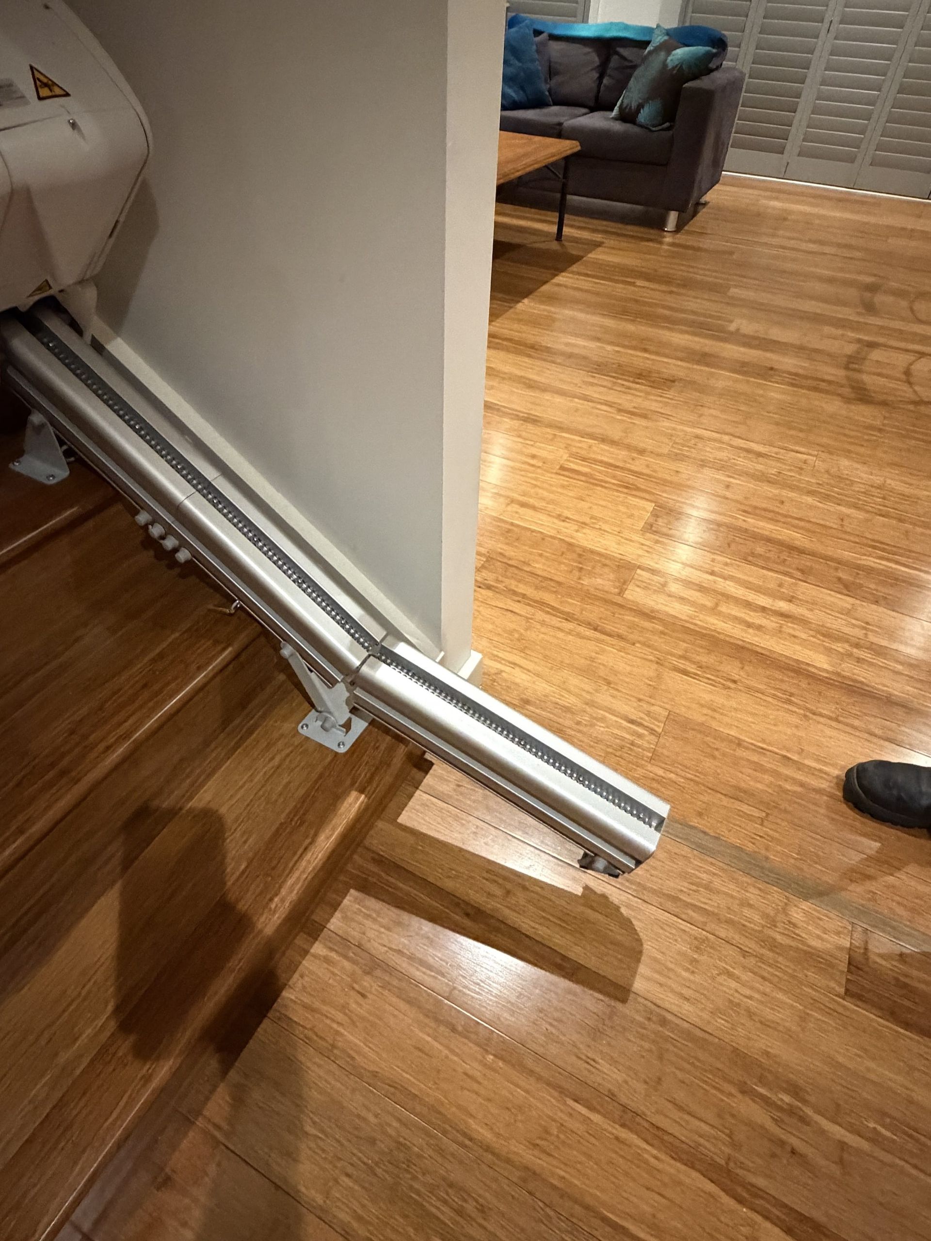 Silver wall-mounted folded gate/ramp leaning against a white wall in a hardwood-floored room.