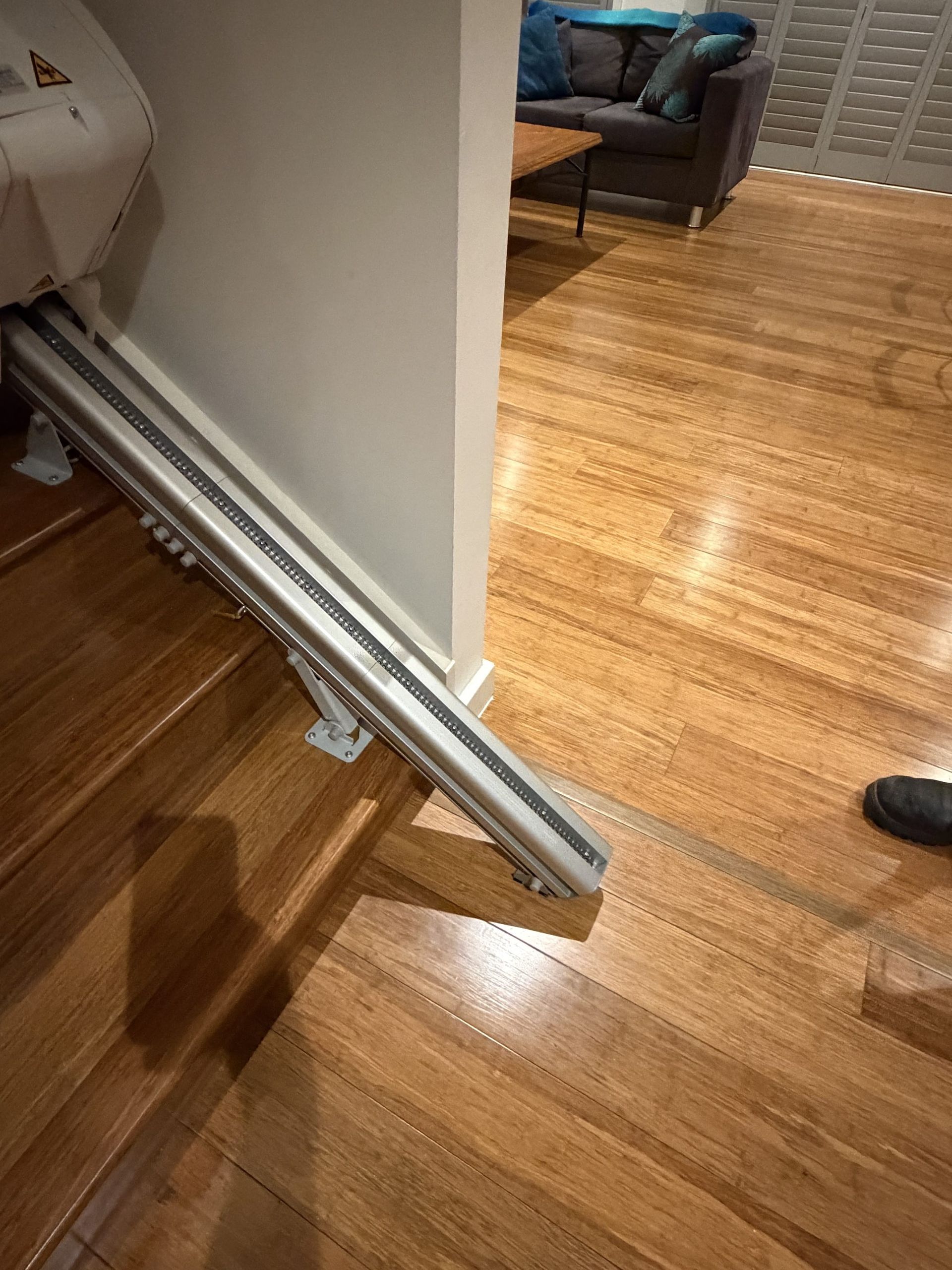 A folding wheelchair ramp at a doorway between wood floors, with a couch in the background.