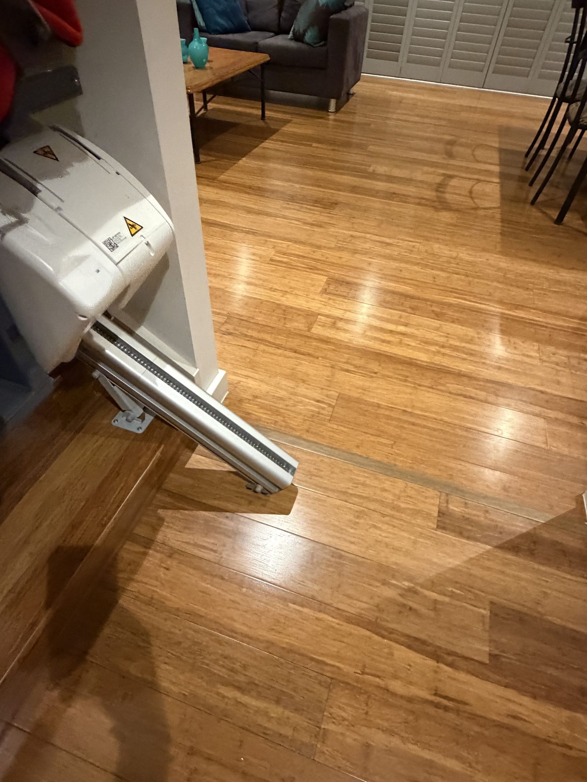 Laundry machine tipped on its side in a hardwood-floored room, with a chair and table nearby.