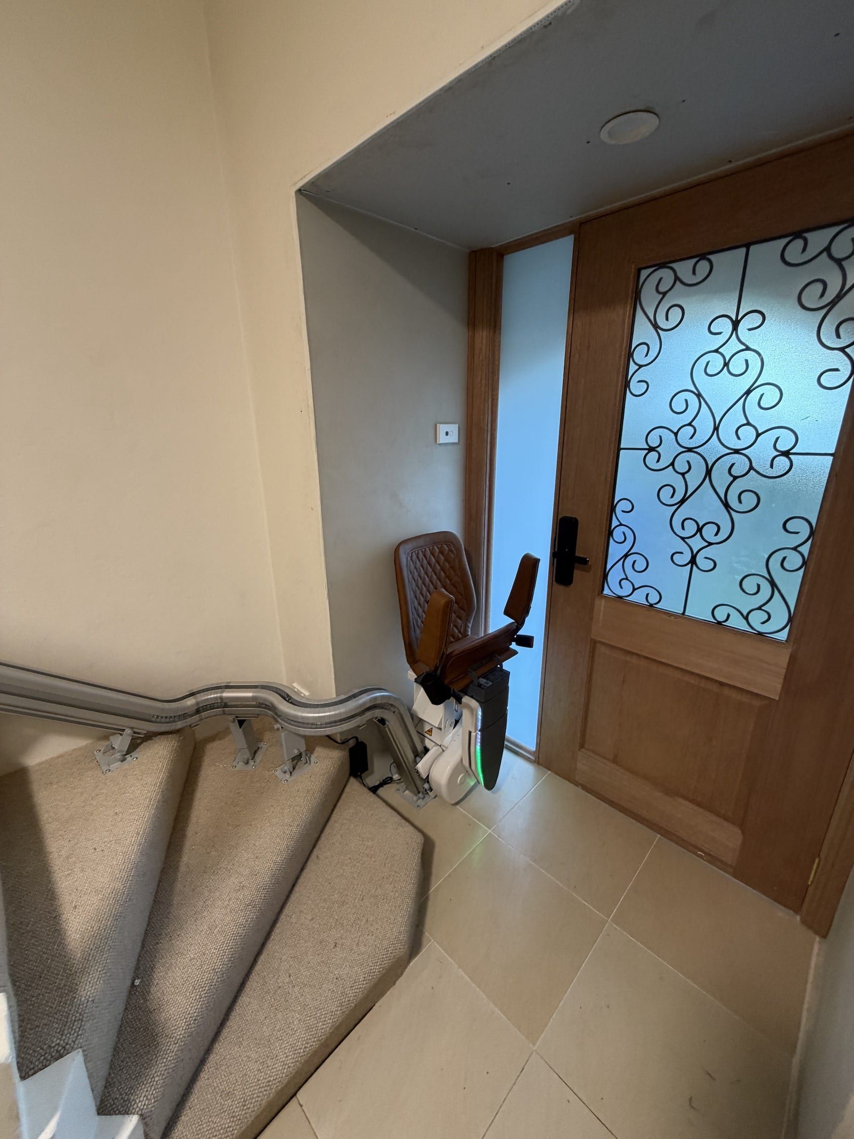 Indoor staircase with beige carpet and wooden door, plus a small dark decorative stand by the entryway.