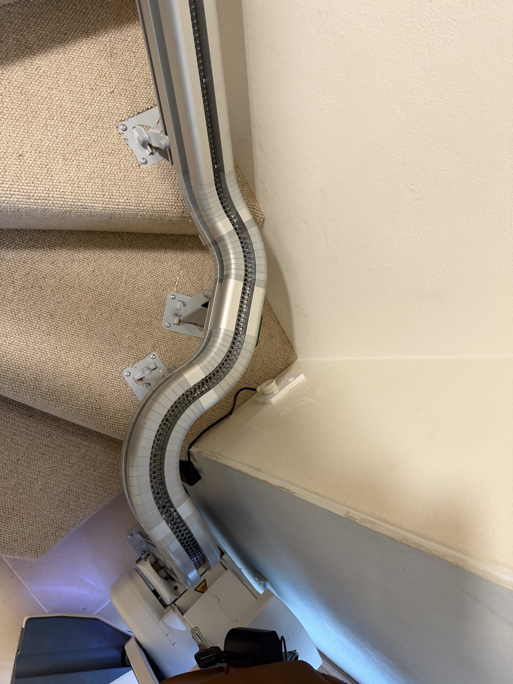 Curtain rail with mounting brackets running along the wall beside a beige window blind and baseboard.