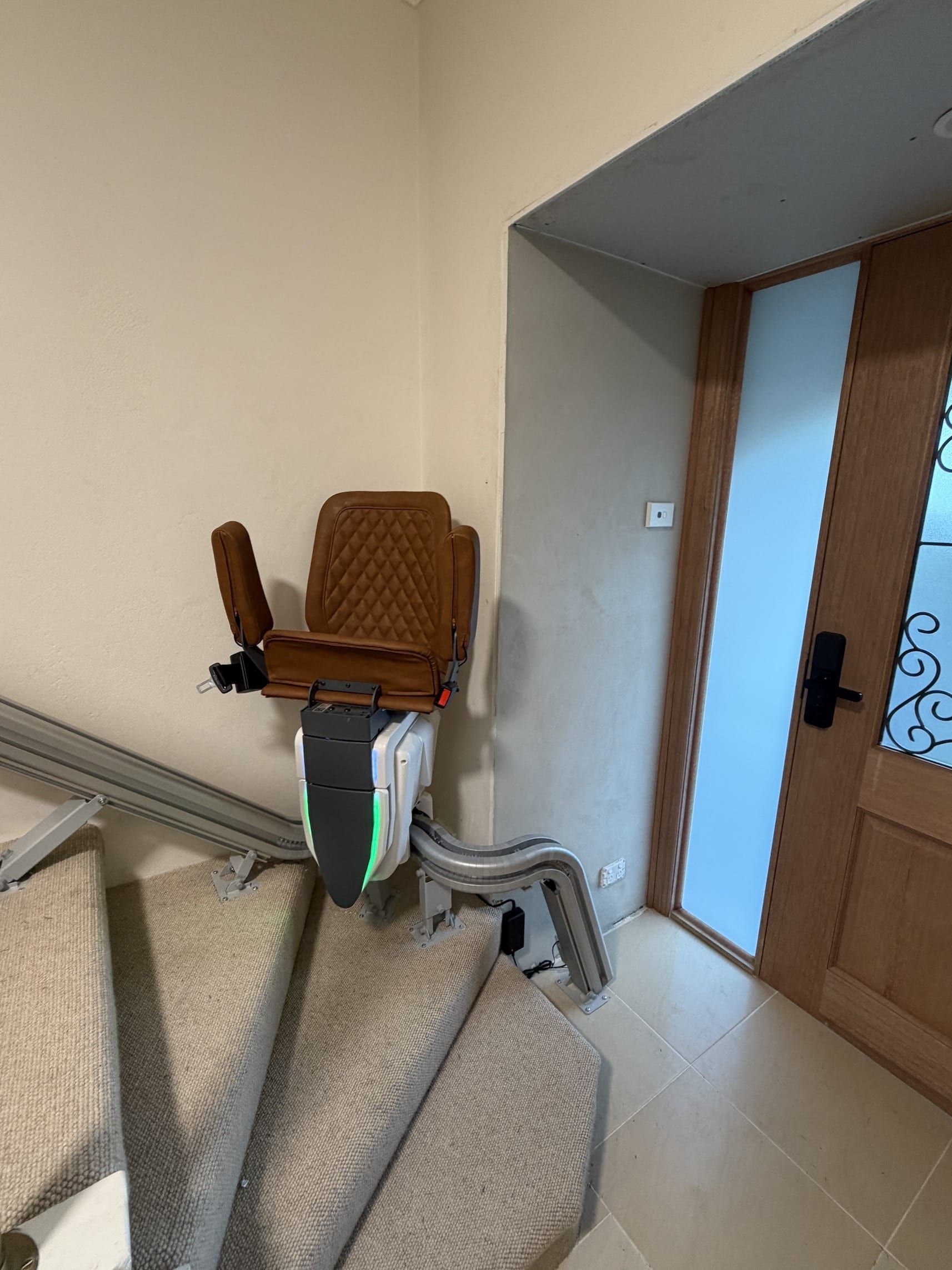 Stairlift beside carpeted stairs in a home hallway near a doorway and wooden doors
