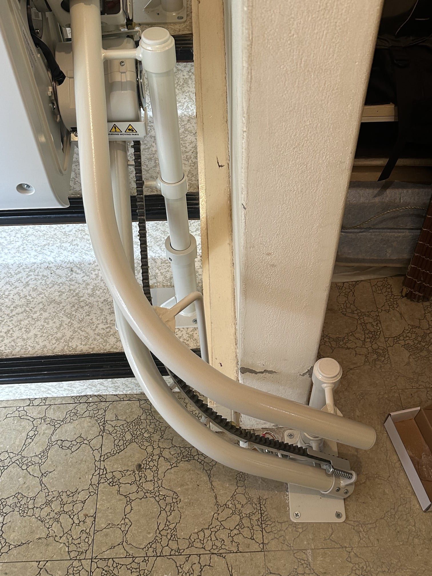 White insulated pipes and cables run vertically along a wall beside a beige carpeted staircase.