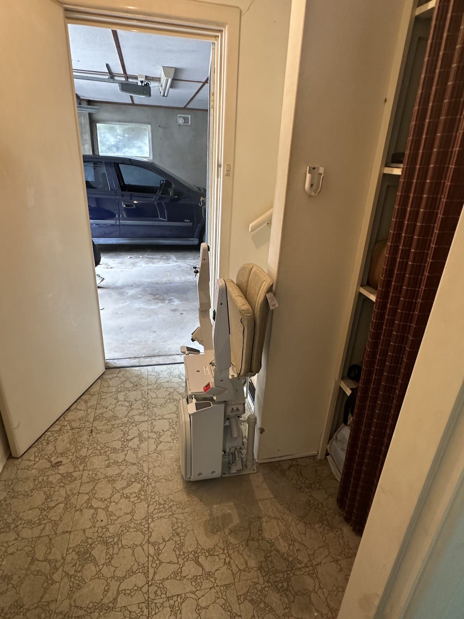 Hallway with a white door open to a garage, a vacuum and box on the floor, and patterned carpet.