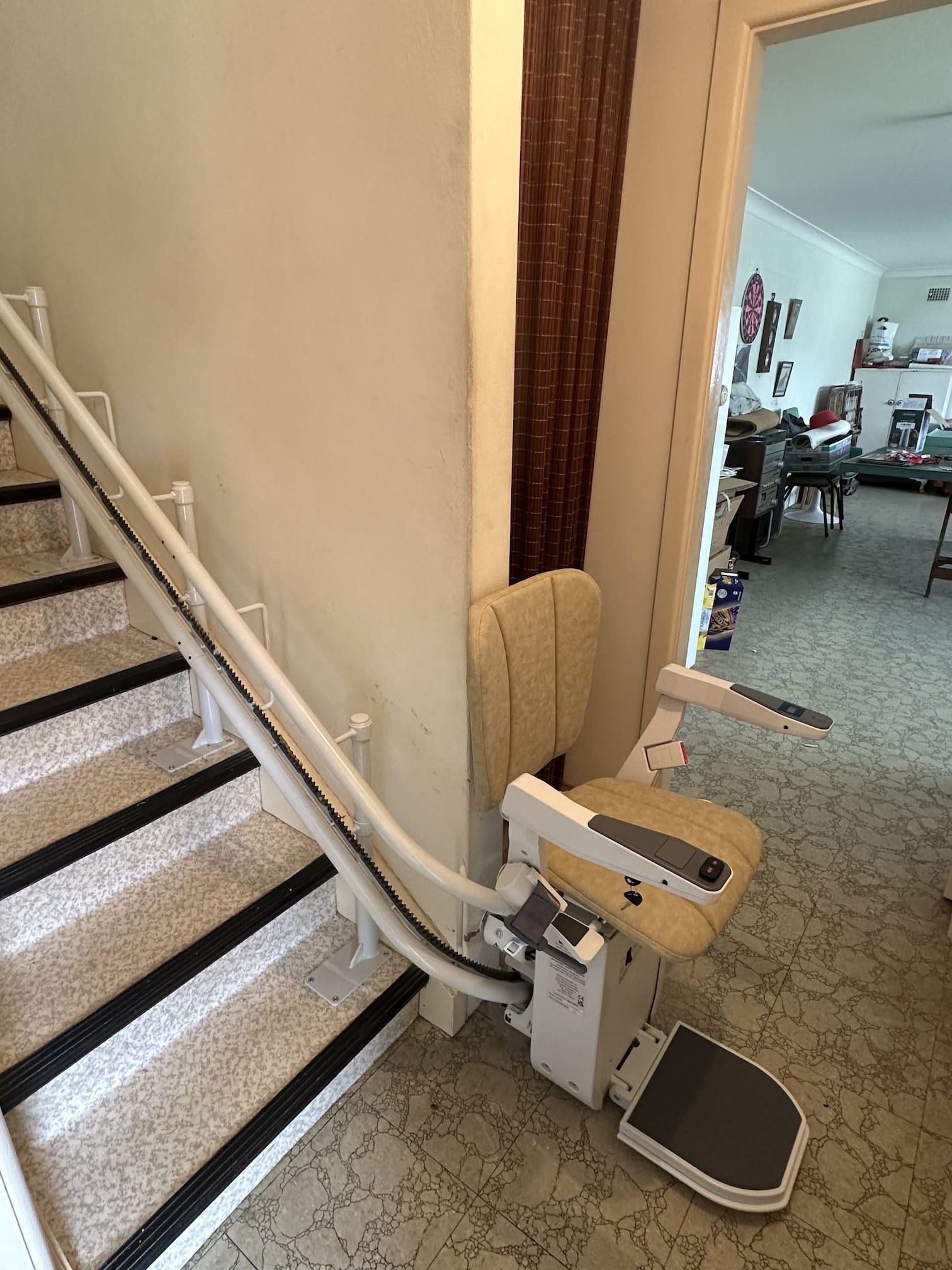 Stairlift on a carpeted staircase beside a doorway, with a small footrest and seat.