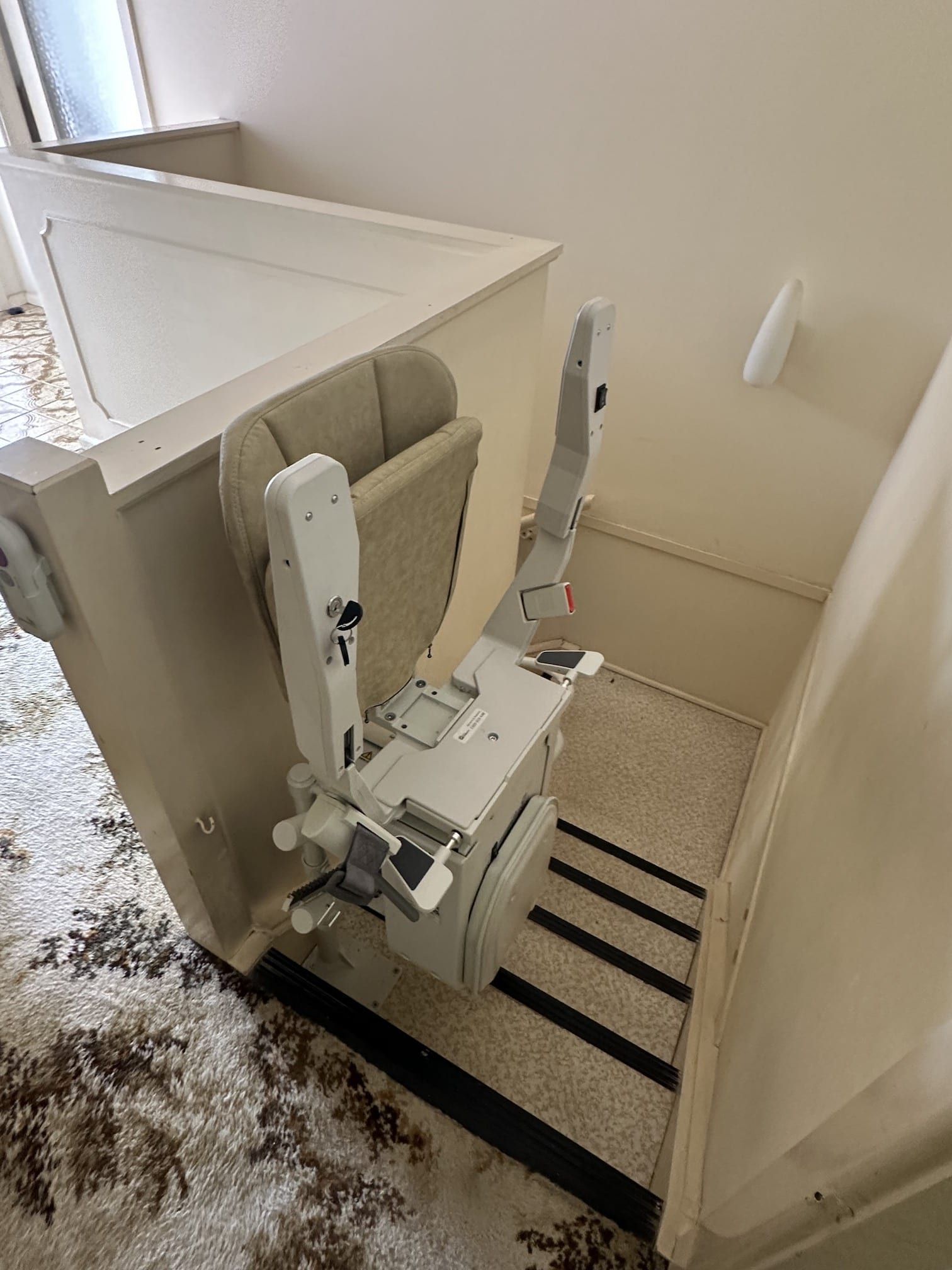 Stairlift installed on a narrow indoor staircase with beige walls and carpet.