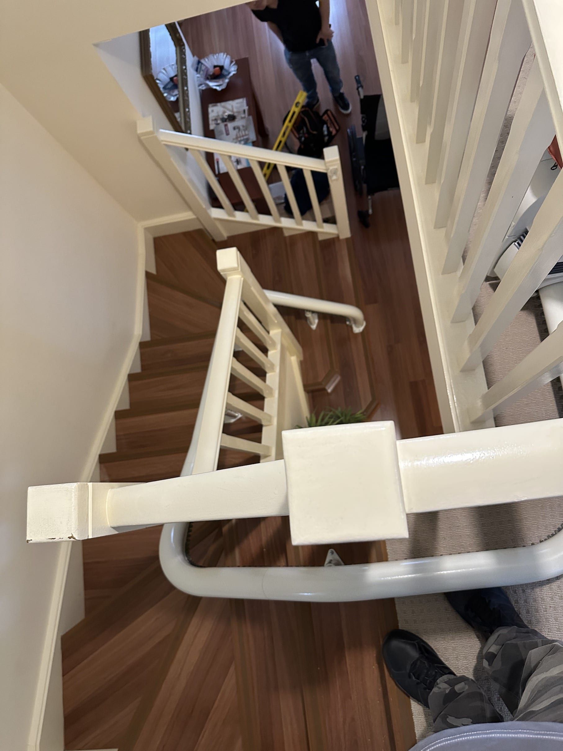 Looking down a narrow wooden staircase with white railings and a ladder-like gate blocking the path