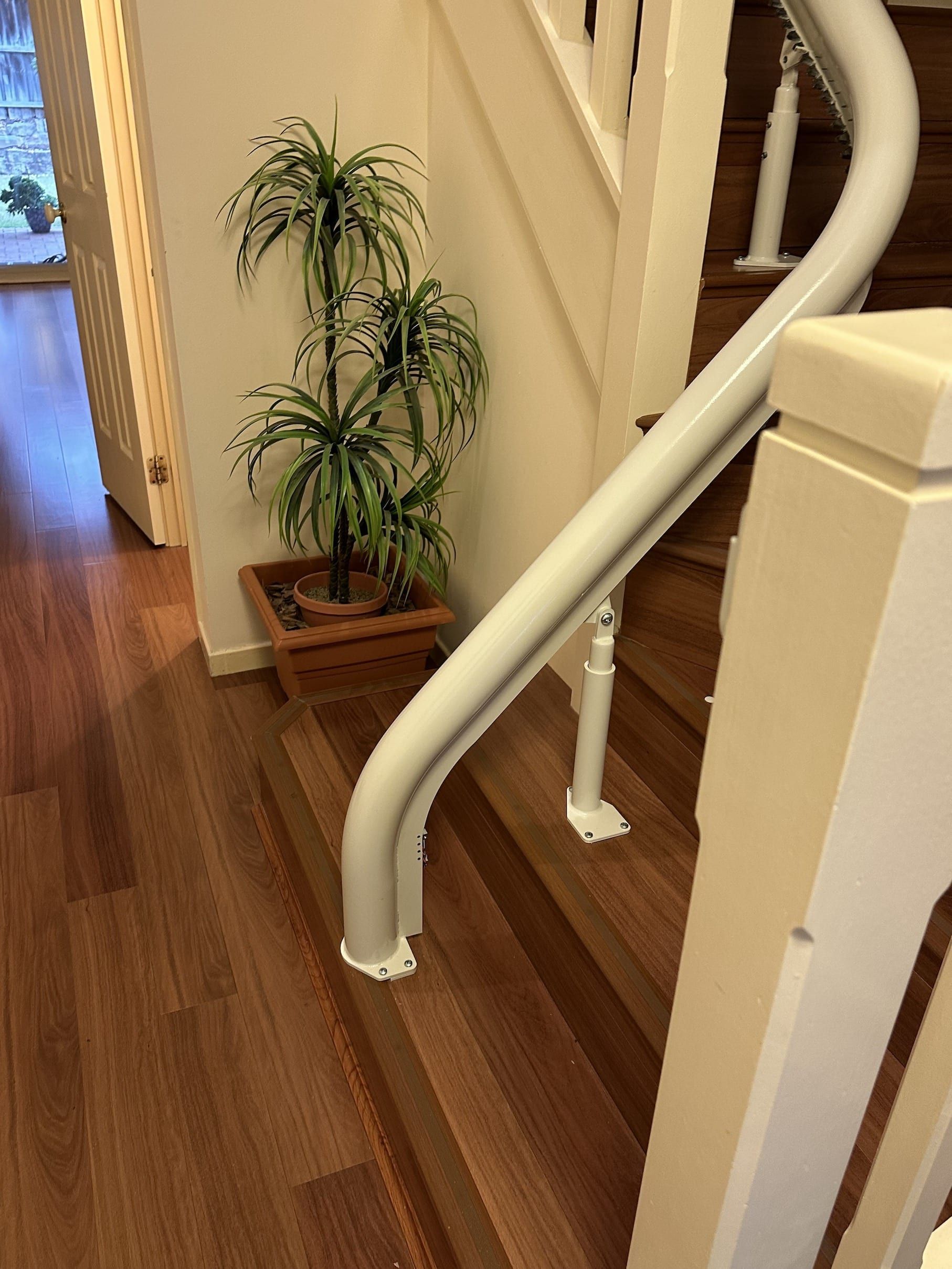 Indoor staircase with white railing and a potted plant beside wooden steps.
