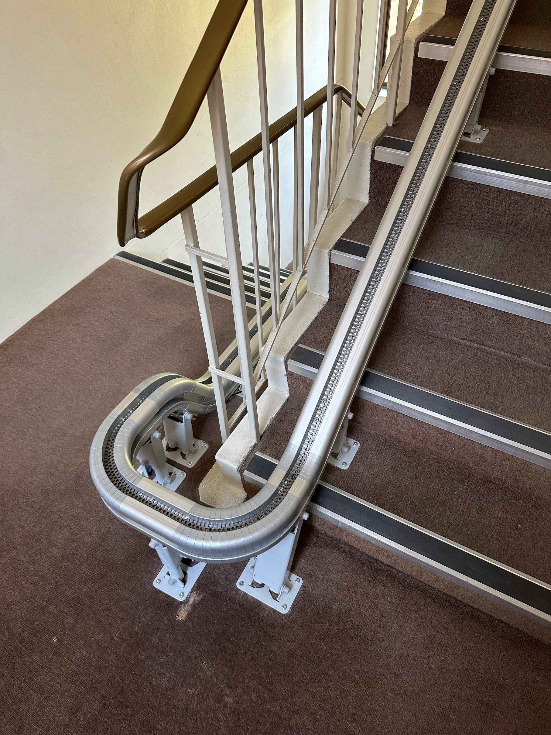 Curved stairlift track with white handrail beside a carpeted staircase indoors